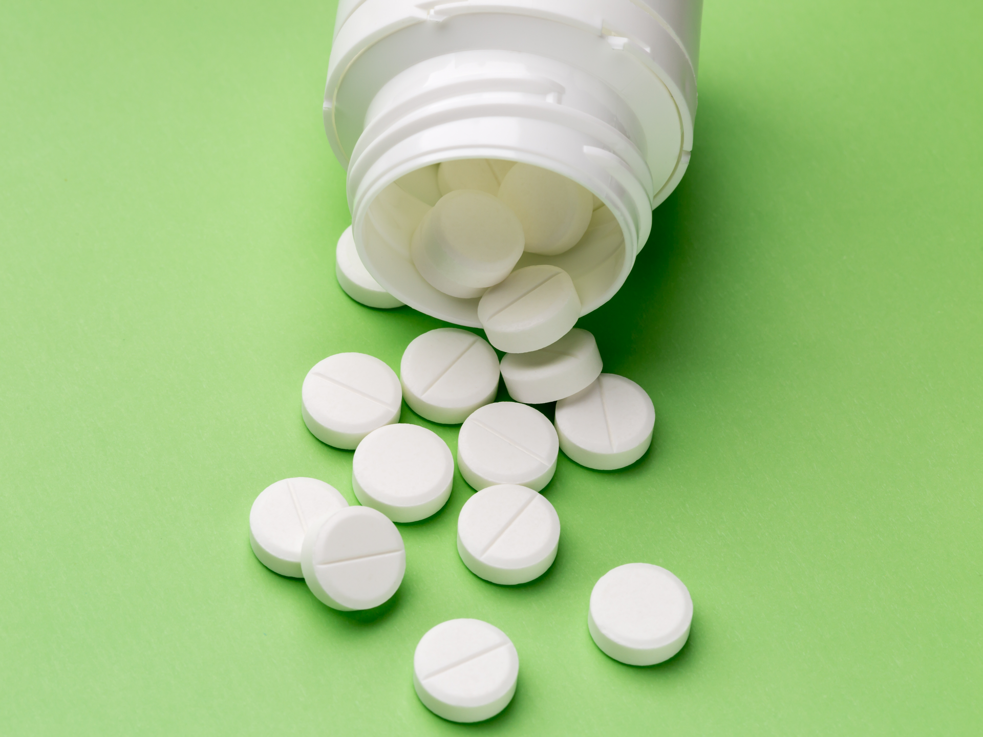 White pills pouring out of a bottle against a green background