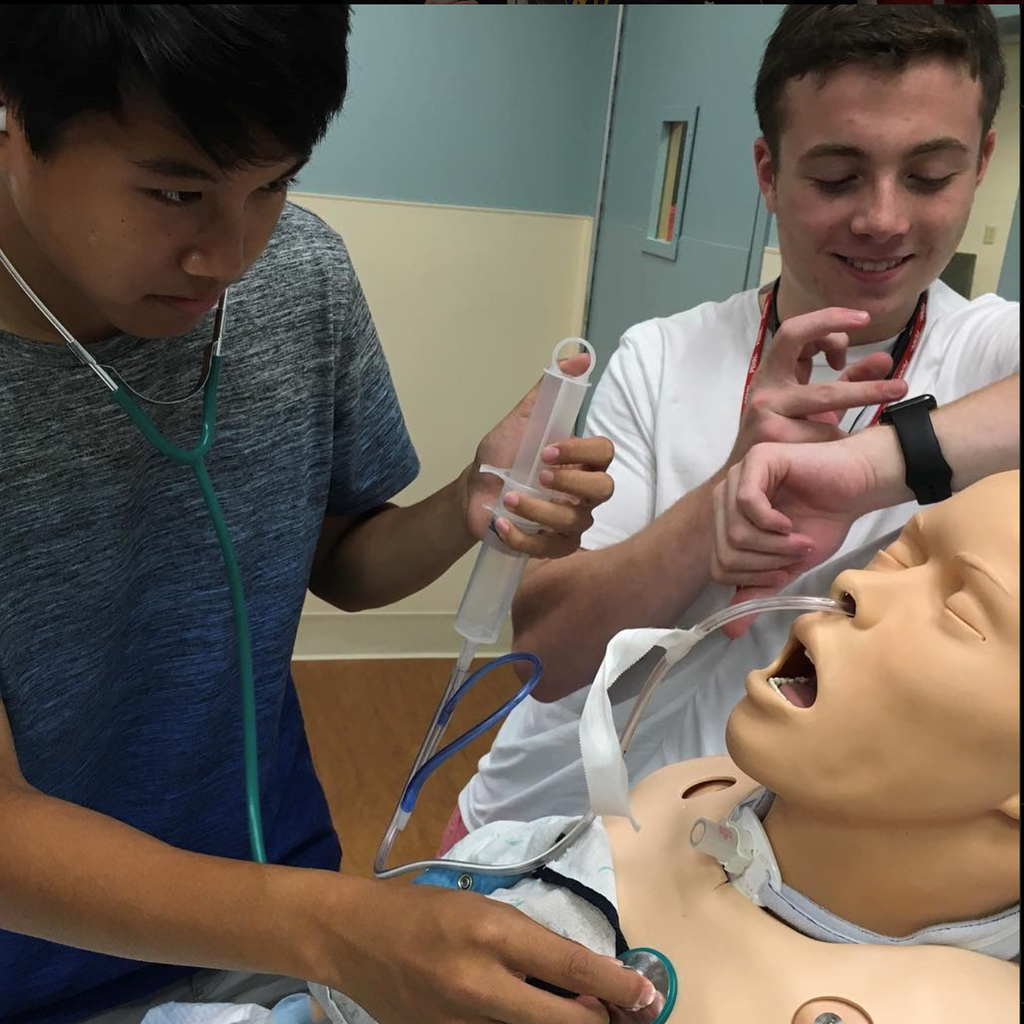 Two students with stethoscopes examine a medical manikin