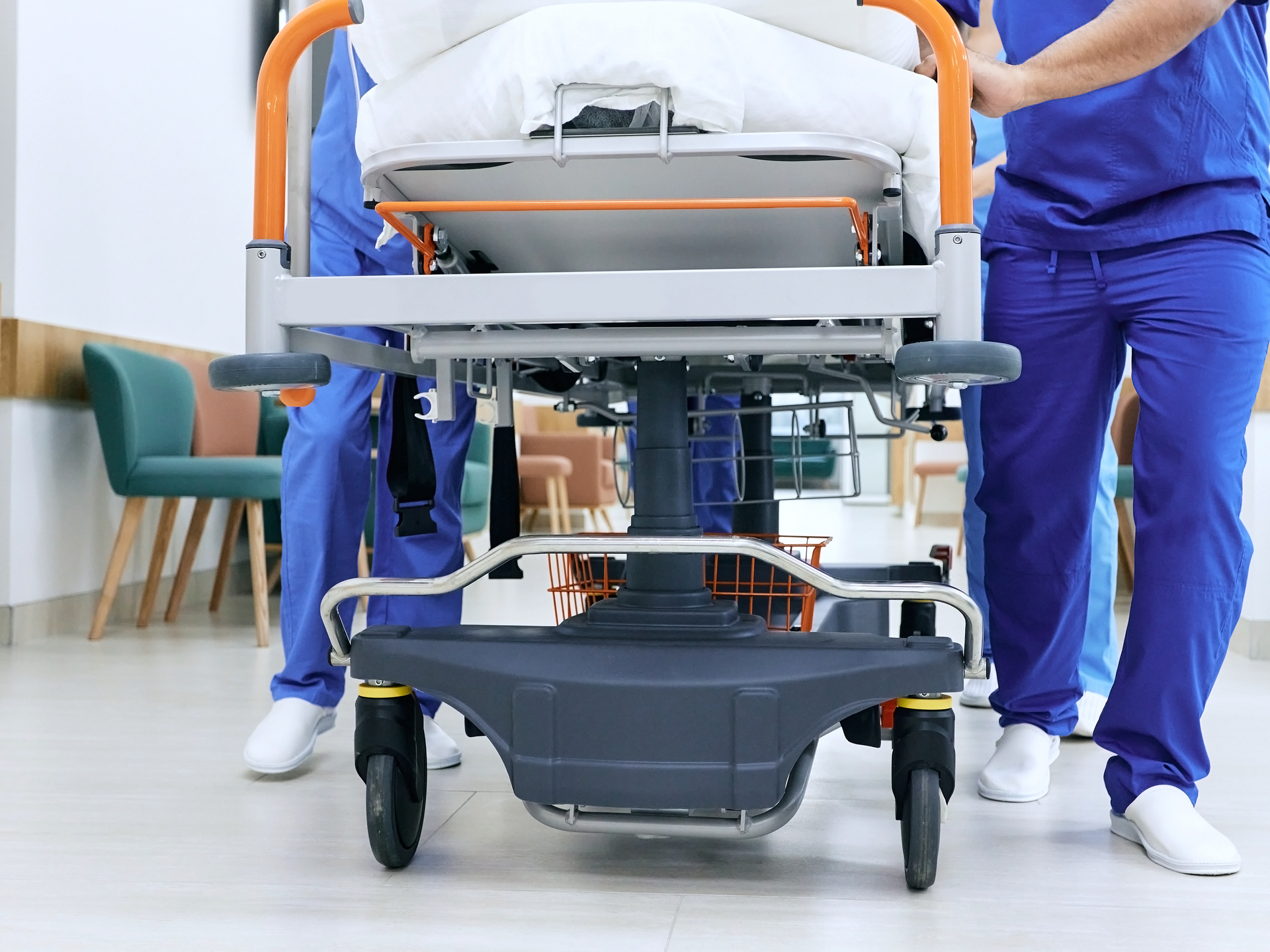 A closeup shot of the legs of medical personnel pushing a gurney down a hospital hallway.