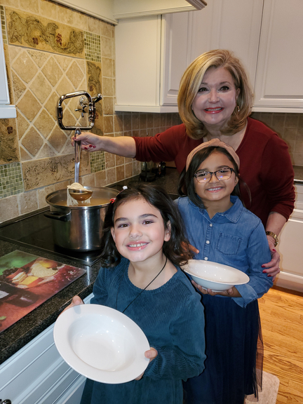 Pat Ciarrocchi with two young girls in the kitchen, posing with plates and a pot of spaghetti 