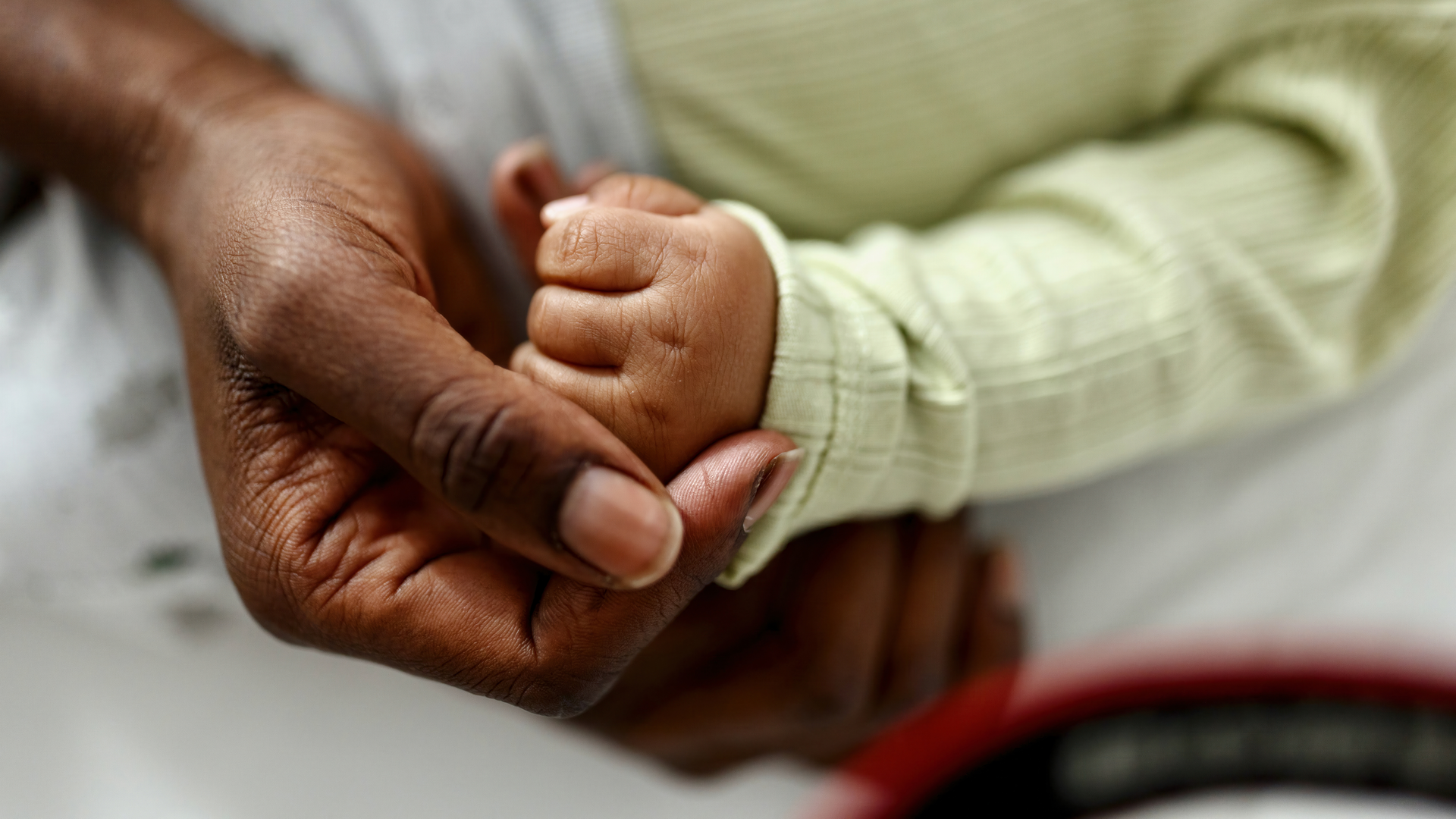 Close-up of a Black woman's hand holding a baby's small fist in her palm