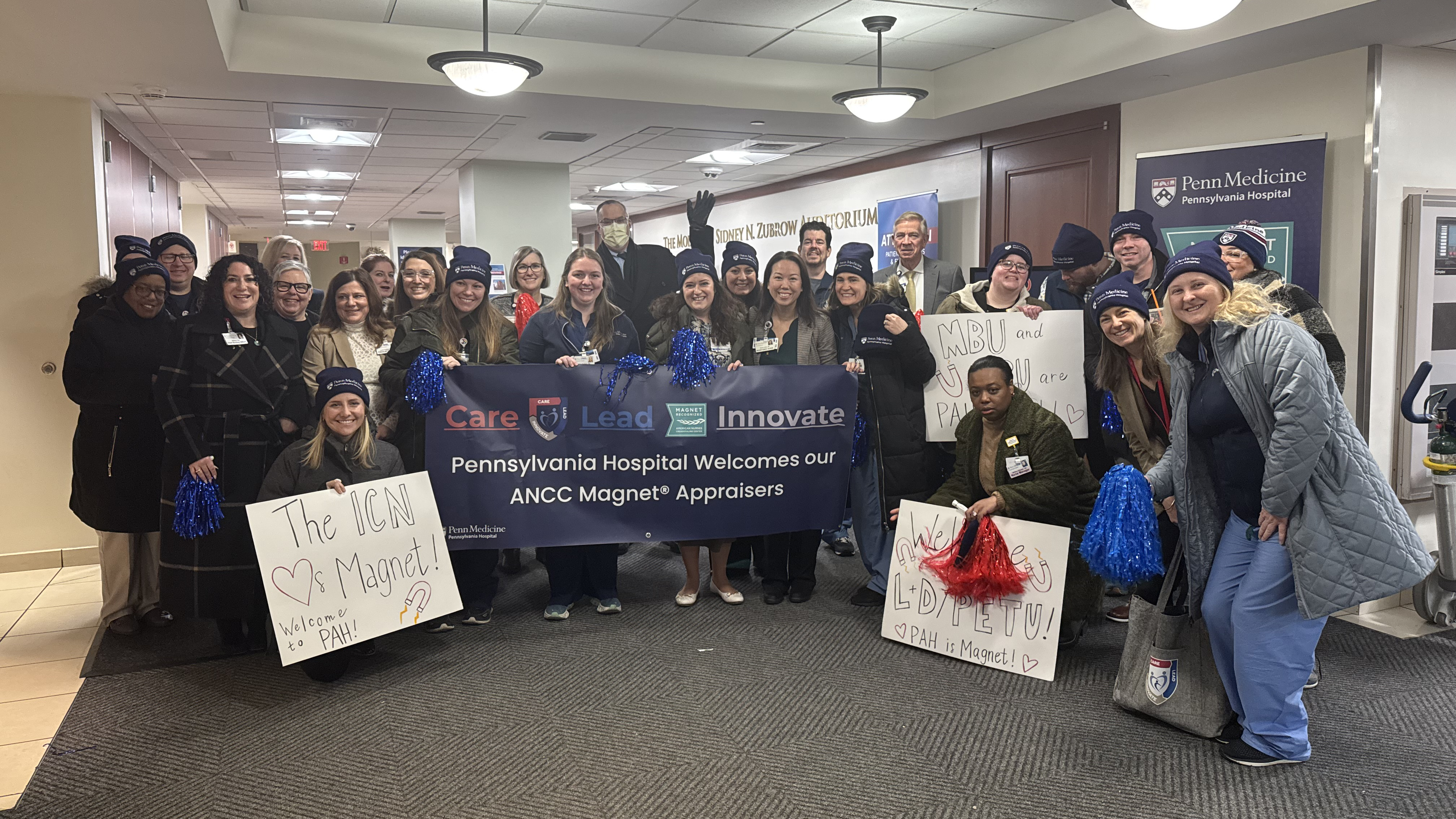 A group of employees holding red and blue pom-poms and welcome signs at Pennsylvania Hospital’s entrance