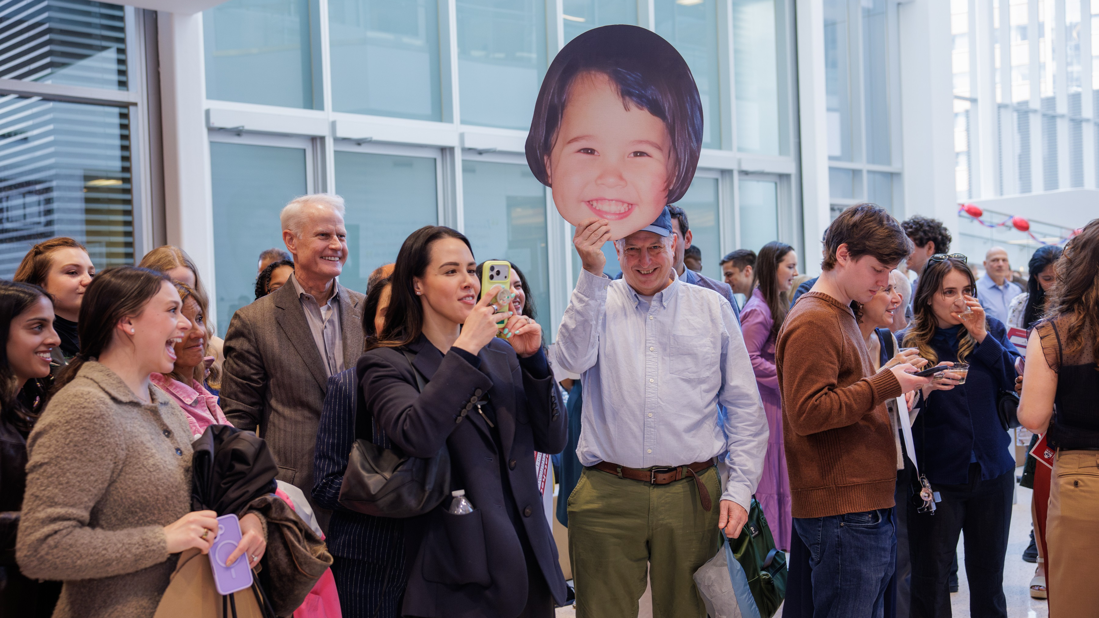 Proud families and friends celebrate their loved ones matching into residency programs. One man holds a giant cardboard cutout of a medical student’s face when they were a child