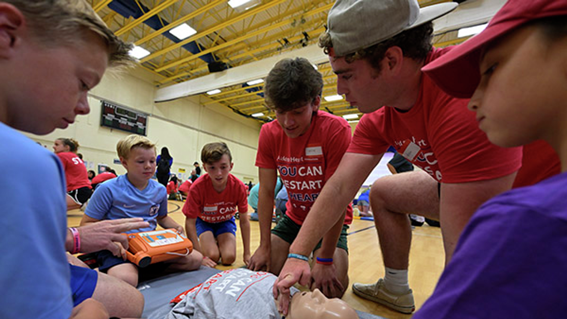 Children watching CPR demonstration Hands-Only CPR class in gymnasium. 