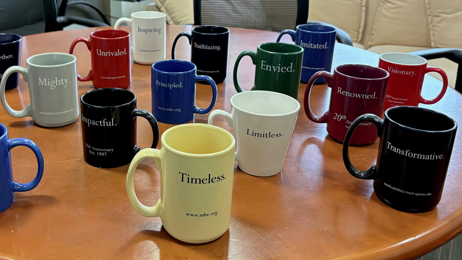 Colorful coffee mugs on a round table, each printed with words like Essential, Timeless, and Trailblazing
