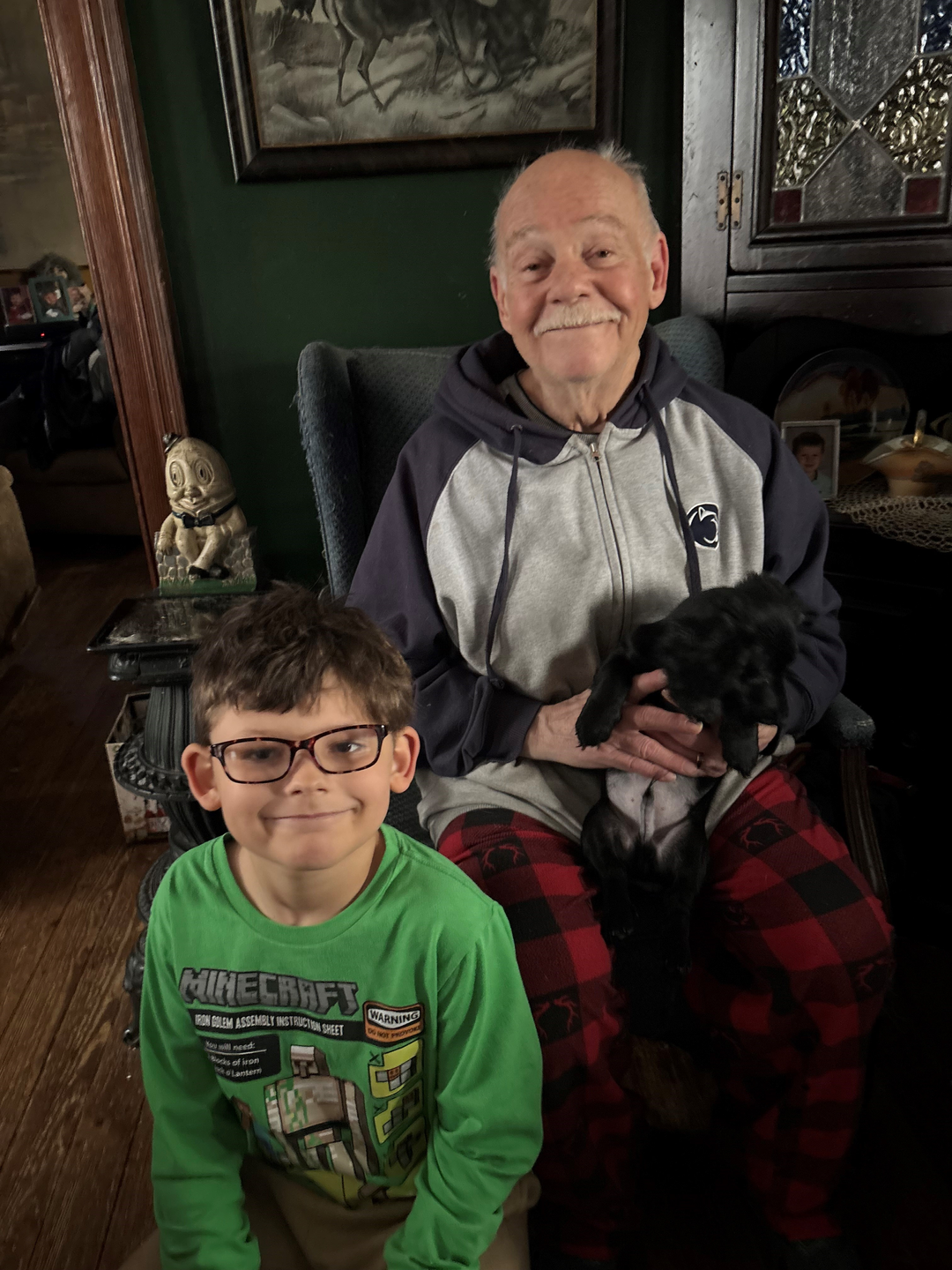 Ed Crane and his grandson sit in their living room, Ed holding a puppy