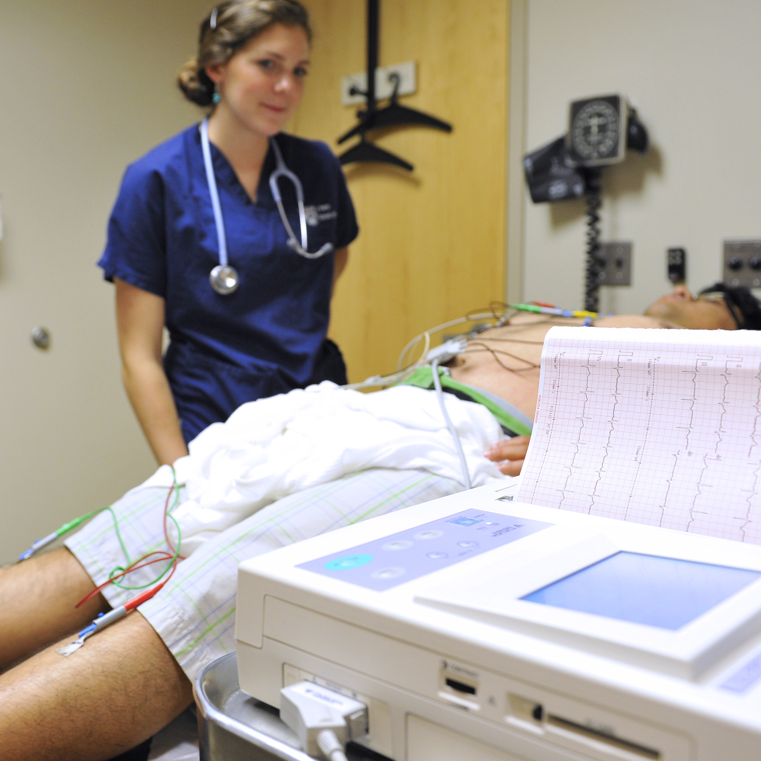 A patient lying on an exam table with electrode sensors attached to his body with a doctor monitoring a printed readout