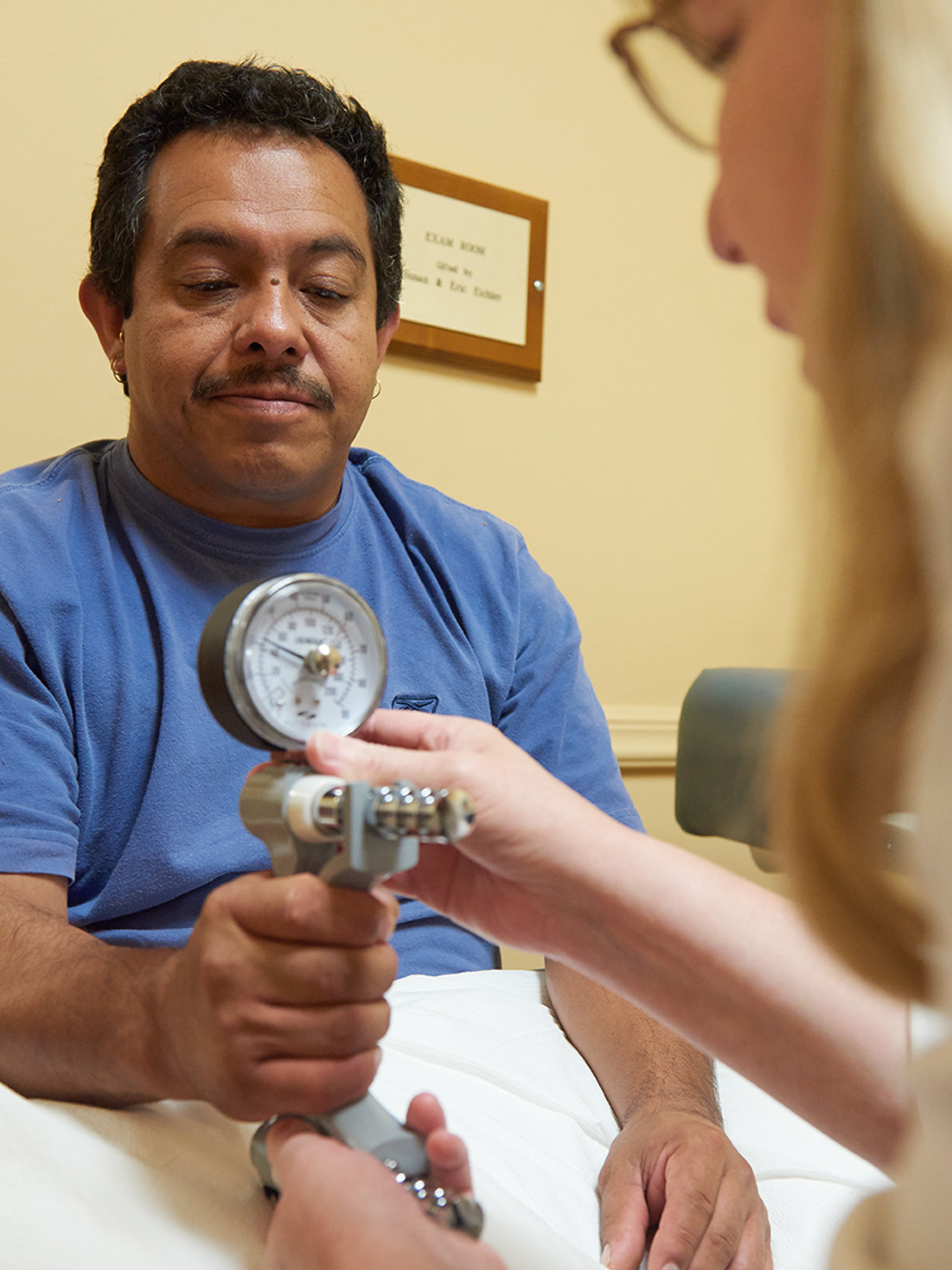 A man holds a machine that appears to gauge his grip strength, while a female therapist takes its reading