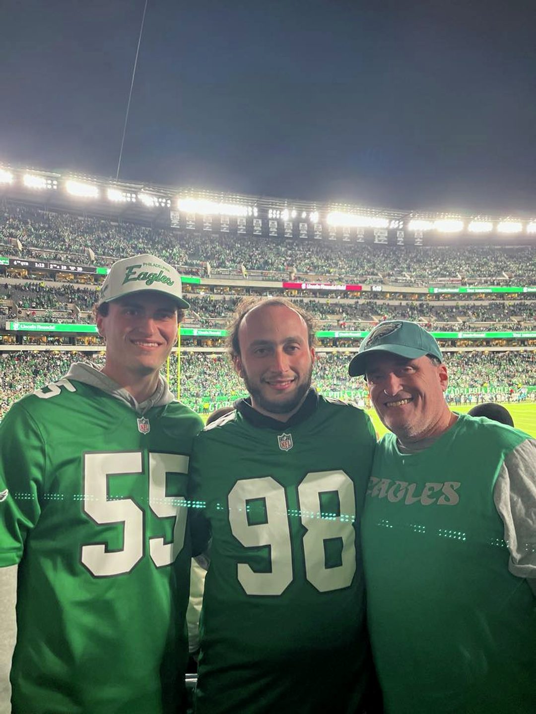 Curt Krouse with two young adult sons wearing Eagles jerseys at a game