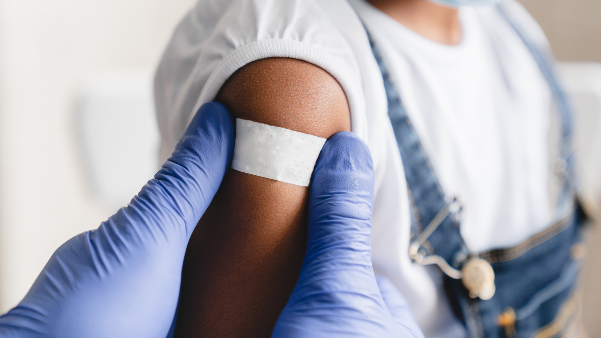 A young girl just got her measles vaccine and a nurse is applying a band aid on her arm.