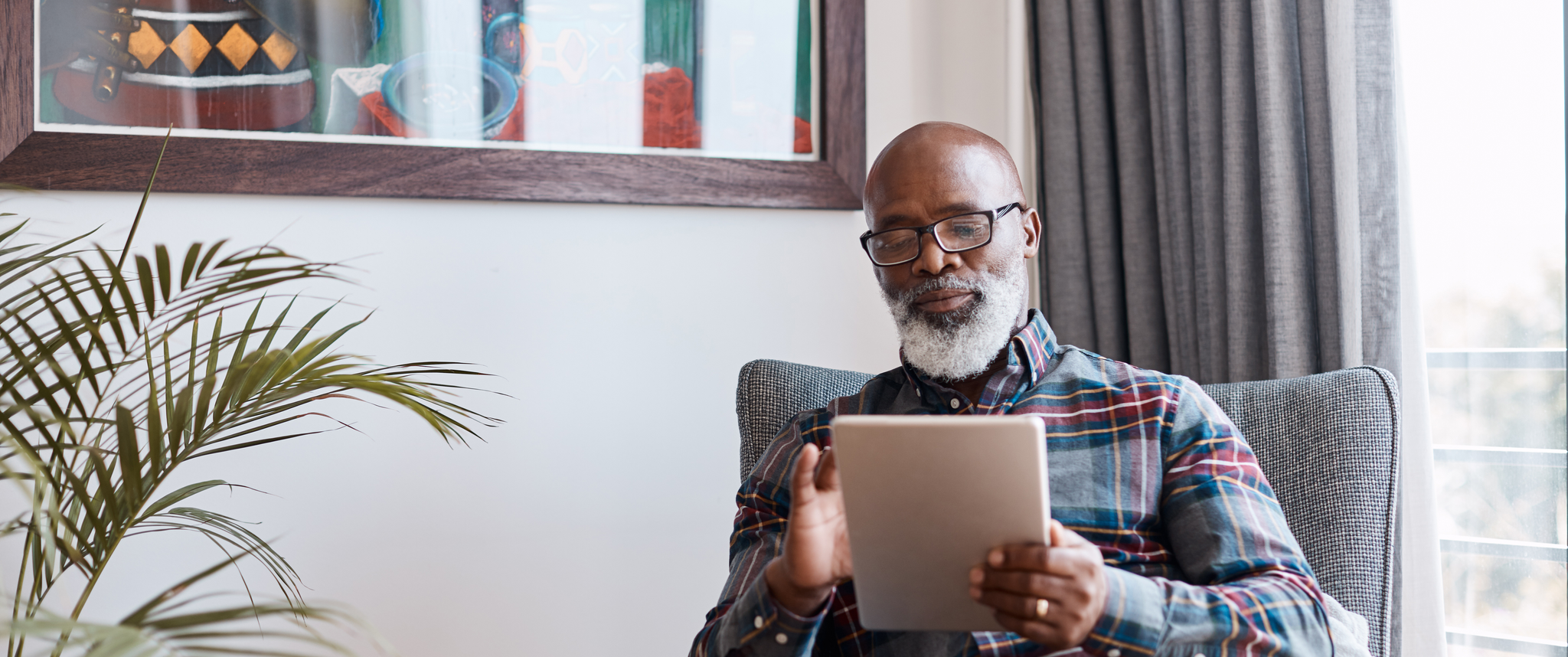 An older man sitting in his living room watching a video on his tablet.