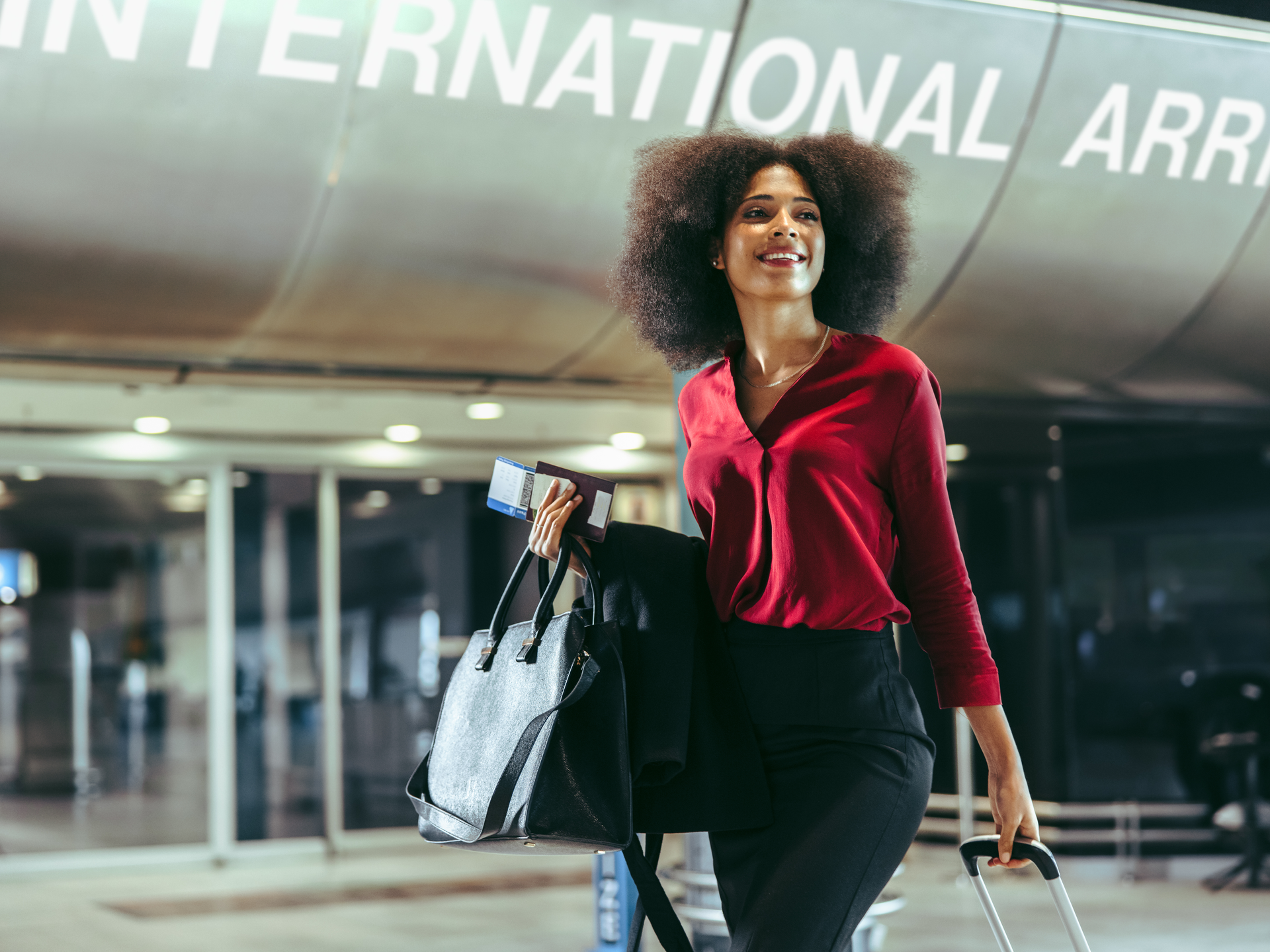 A woman standing with her suitcase and purse in front of a building reading "International Airport".
