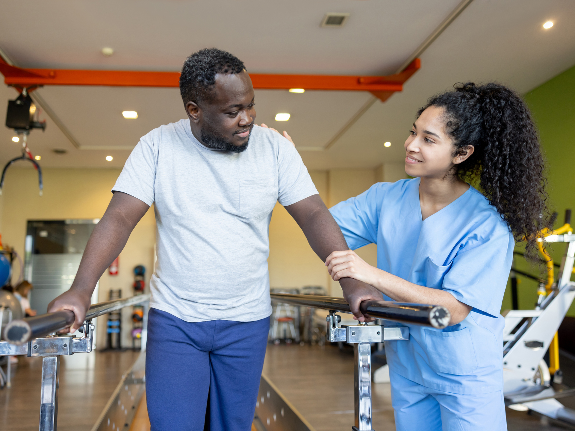 Physical therapy helping an African American man trying to walk on the bars.