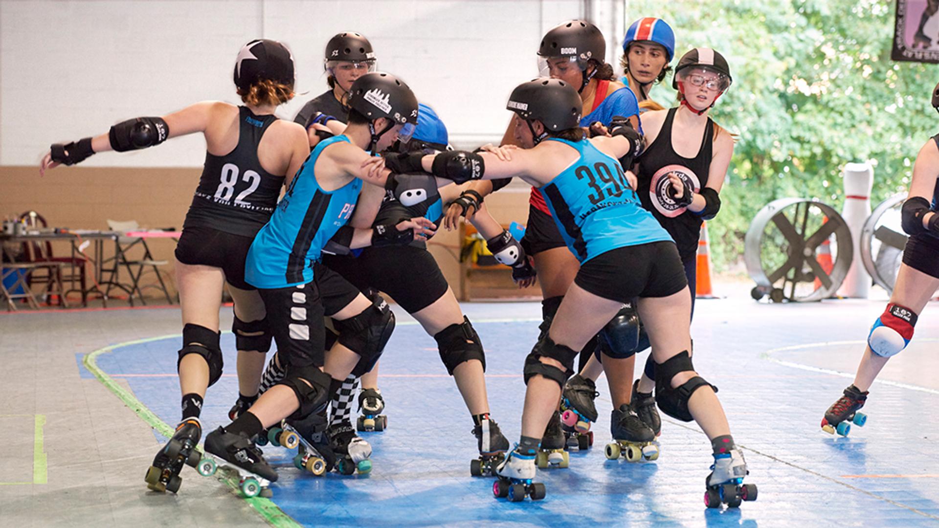 Groups of preteen girls in roller skates and protective gear practice wrestling one another in a roller rink