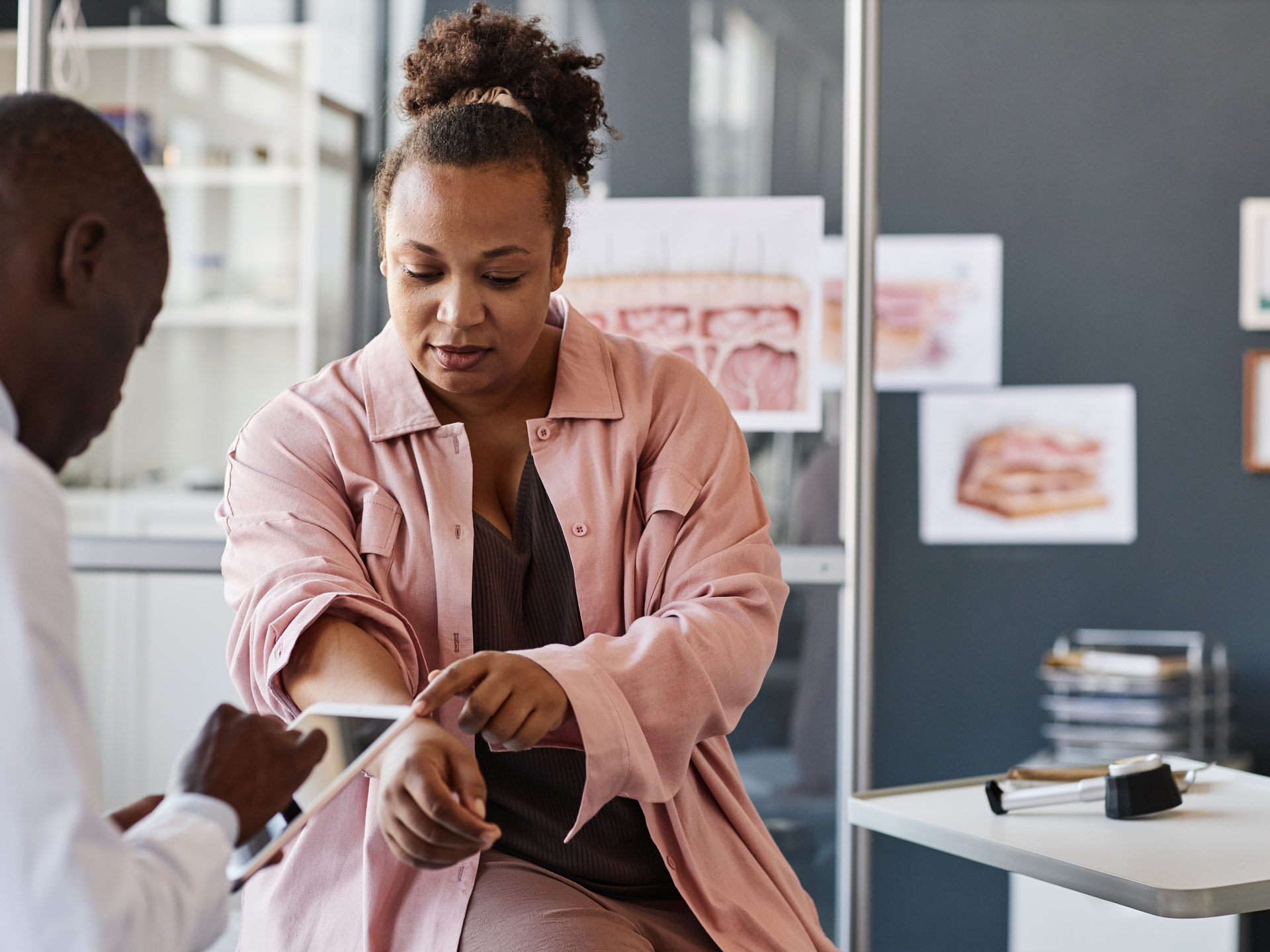 African American woman visiting dermatologist in clinic and pointing at rash spots on hands while explaining symptoms to doctor.