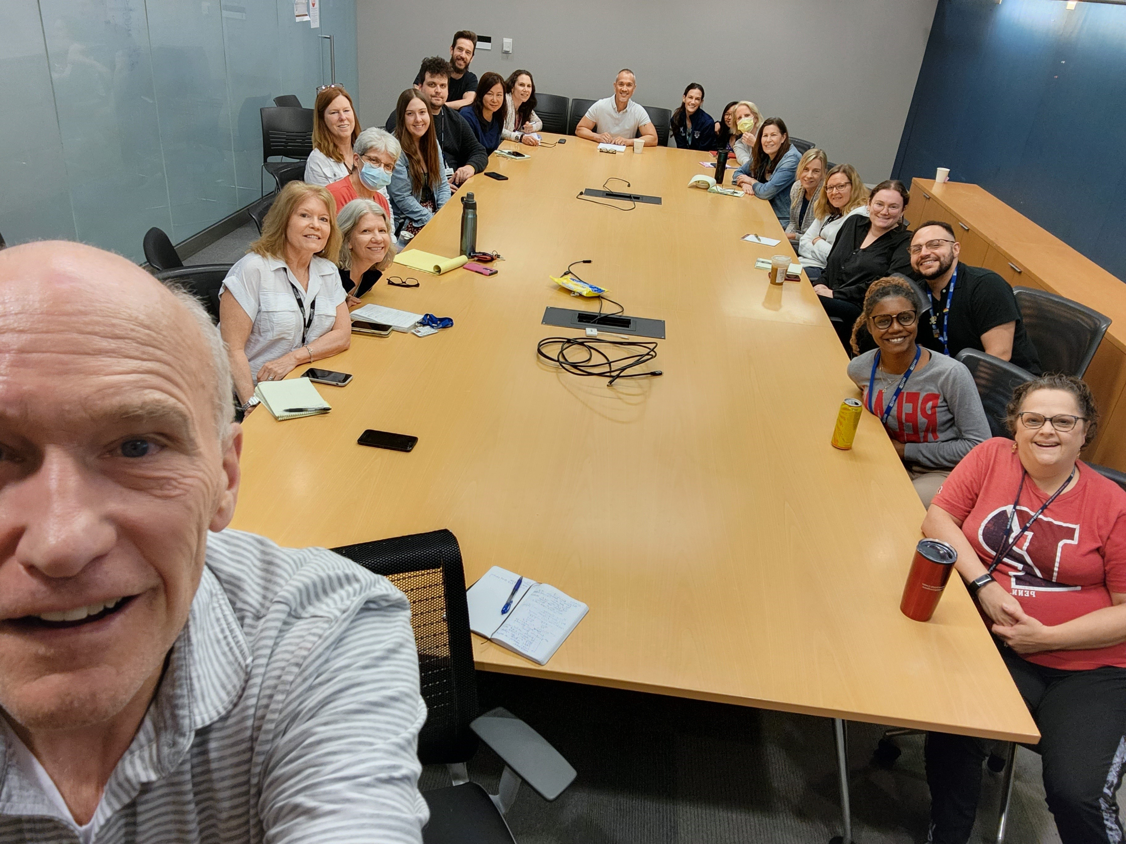 A group selfie taken by Carl June in the foreground with CTU staff arrayed around a conference table behind him, smiling