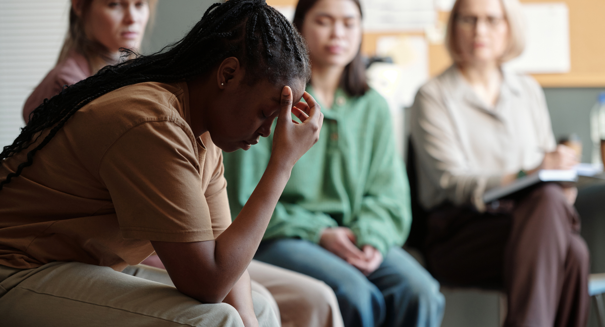 A woman in a support group, looking down with her hand on her forehead