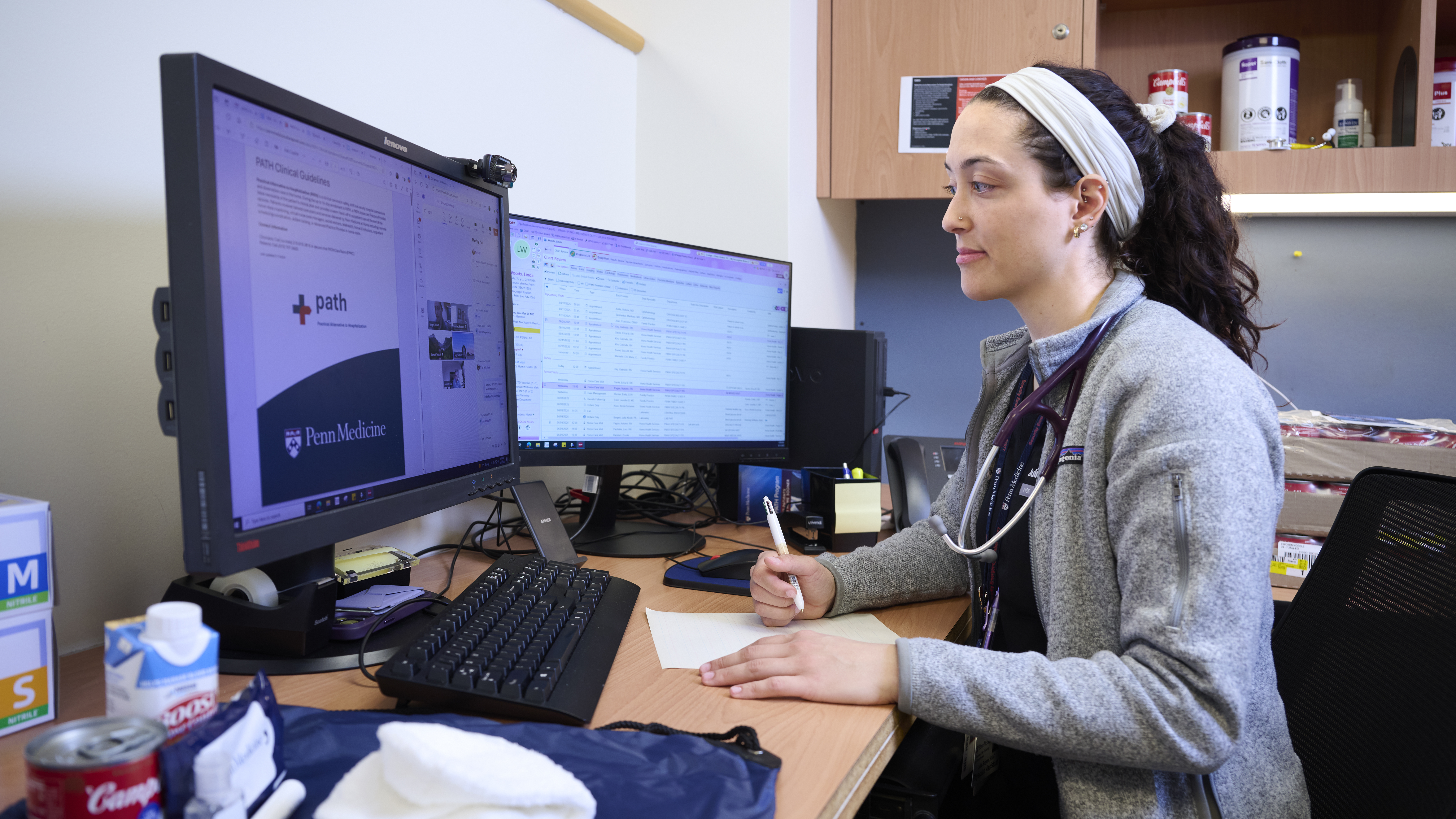 Julia Borgesi sits at her computer attending a virtual meeting, with a care package of goods for patients at the side of her desk