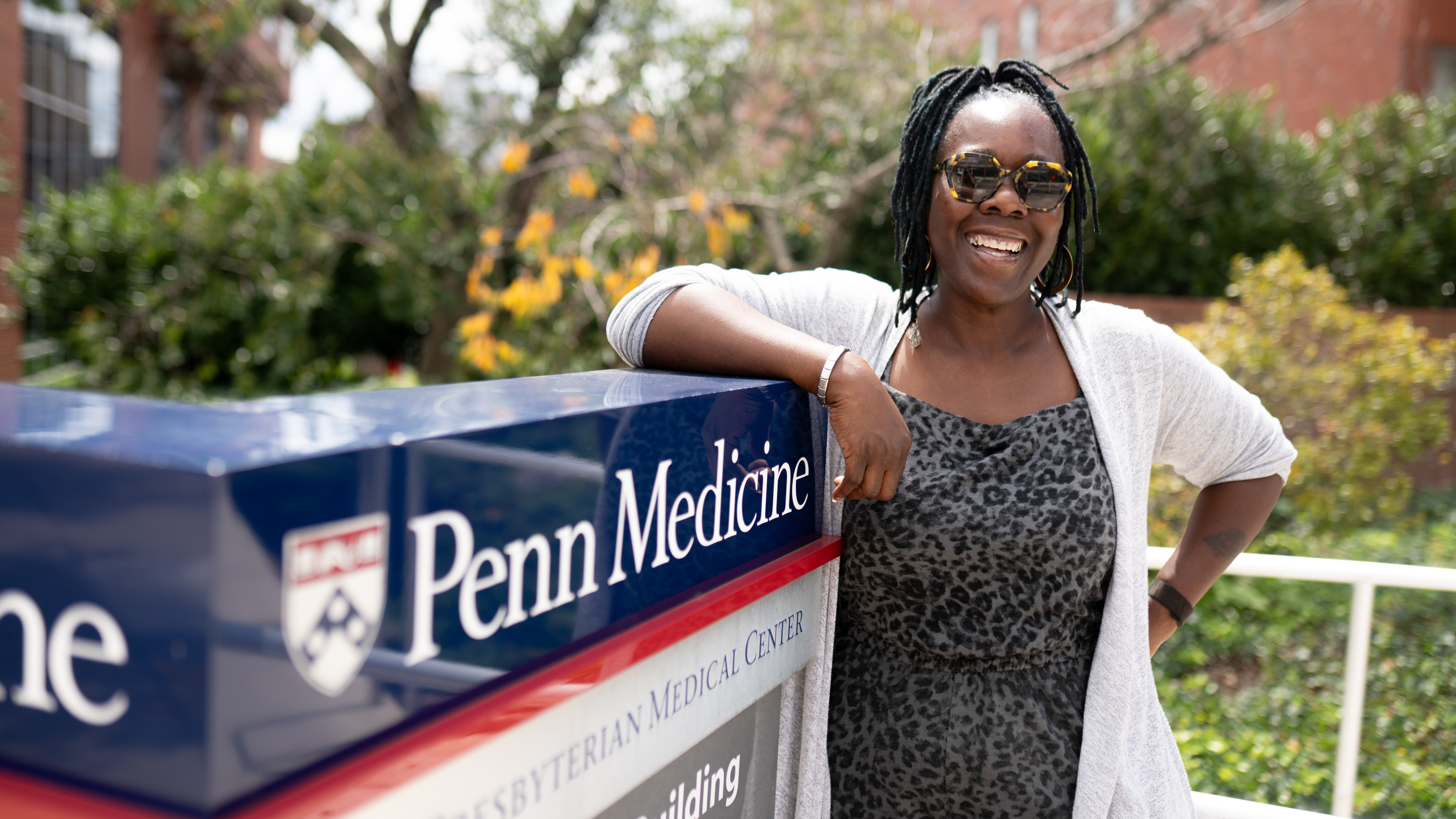 Georgieanna Pierre-Paul standing outdoors beside a Penn Medicine sign with trees and brick buildings in the background