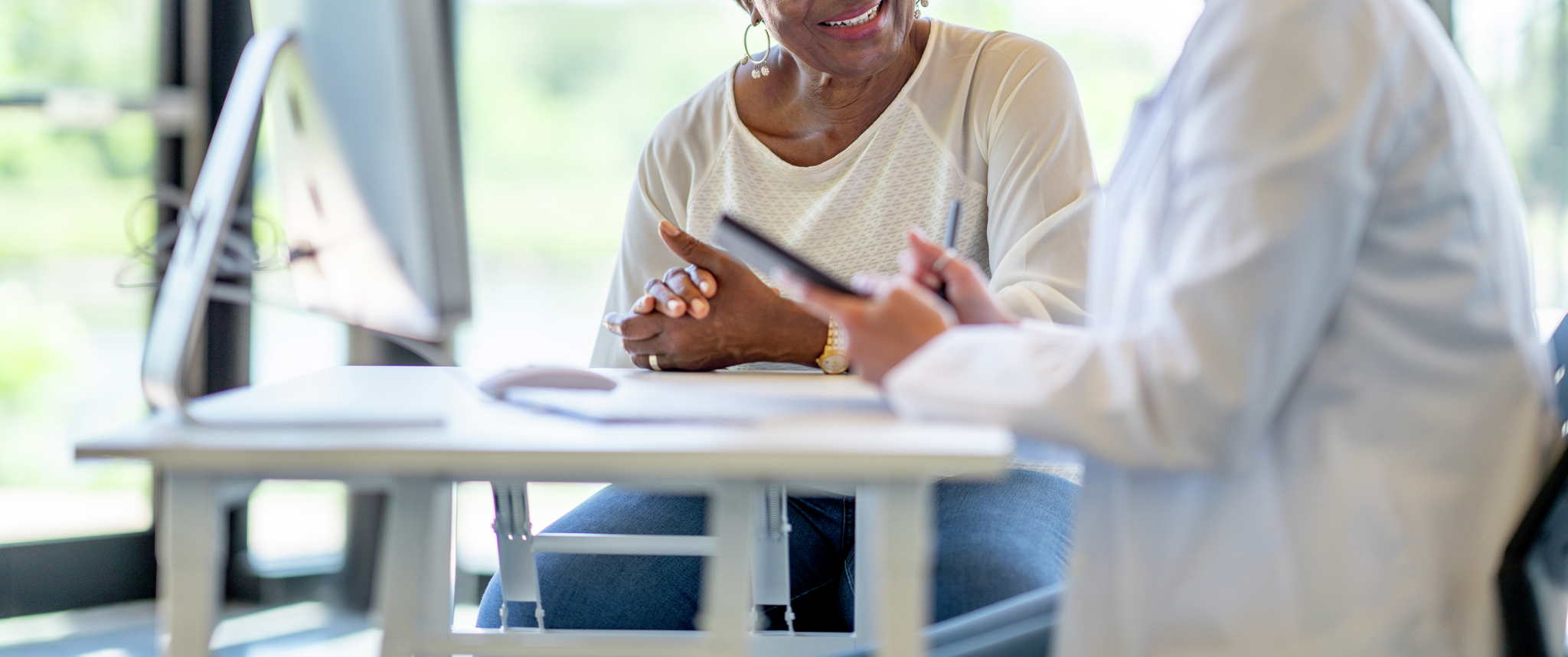 Older Black woman sitting with young doctor at computer desk