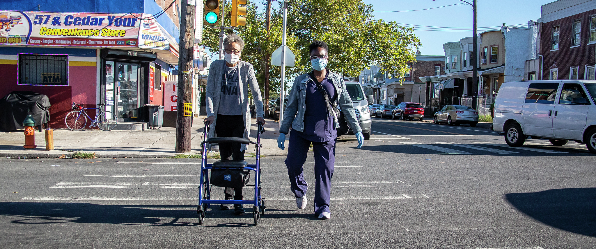 Physical therapist Renee Jones walks with patient Valerie Simon, crossing the street in front of a corner store in Philadelphia
