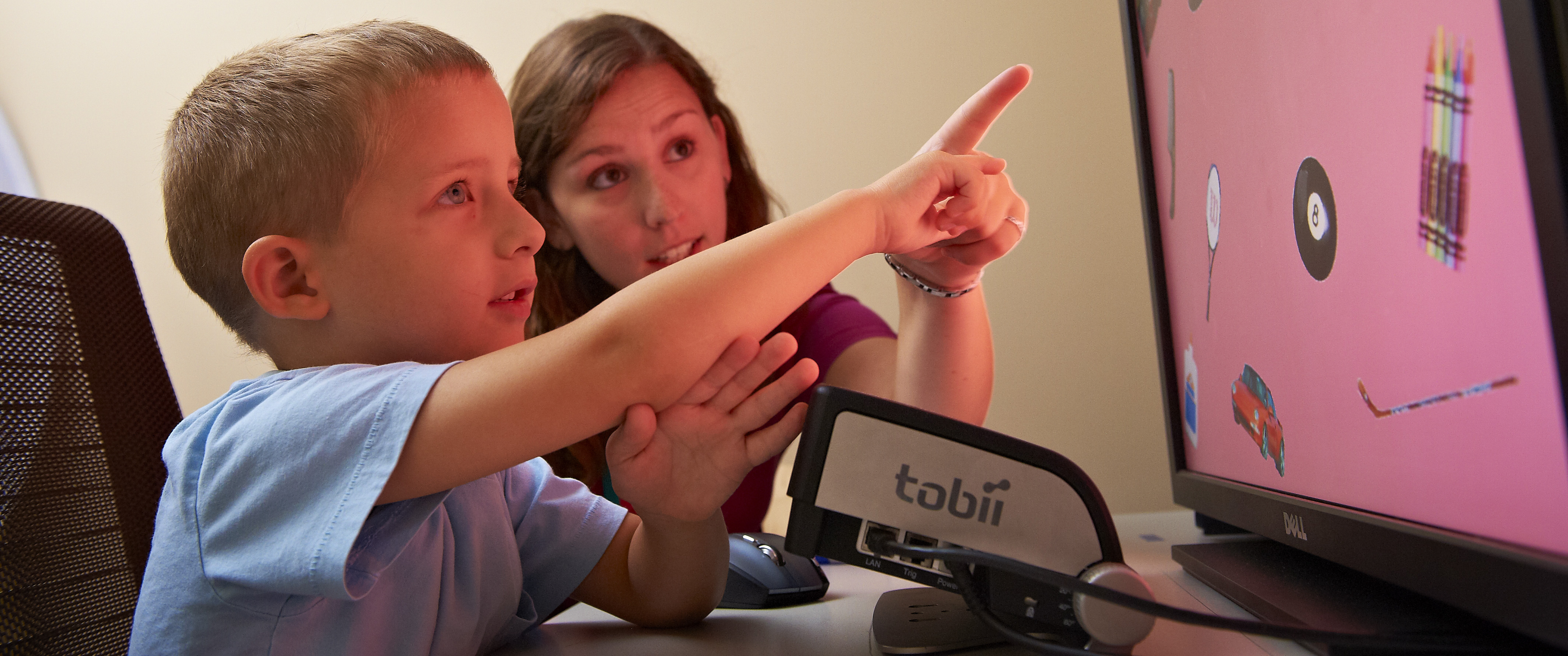A young boy sitting next to an adult points at images on a large computer screen
