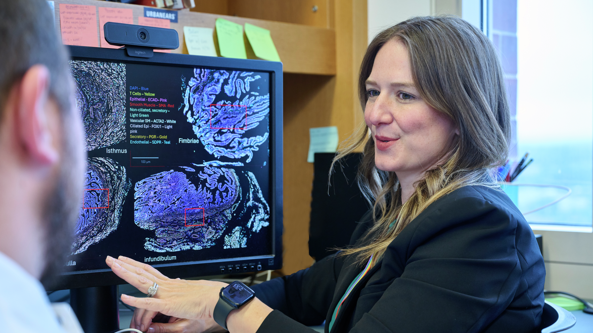 Kathleen O’Neill speaking to a person in a lab, displaying a computer screen with  research graphics.