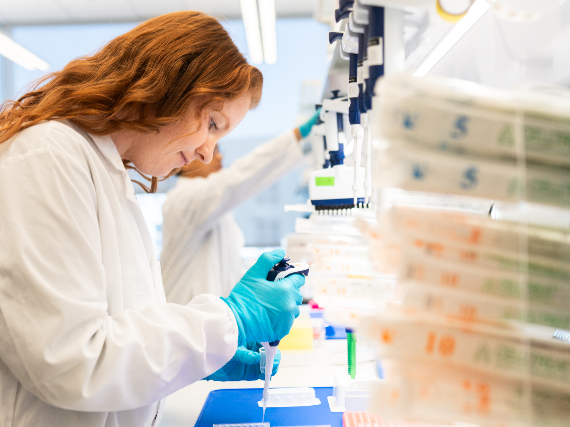 A researcher in a white lab coat uses a pipette at a lab bench
