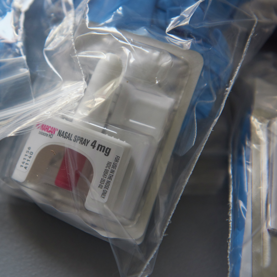 Close up of a baggie of harm reduction supplies including rubber gloves and Narcan