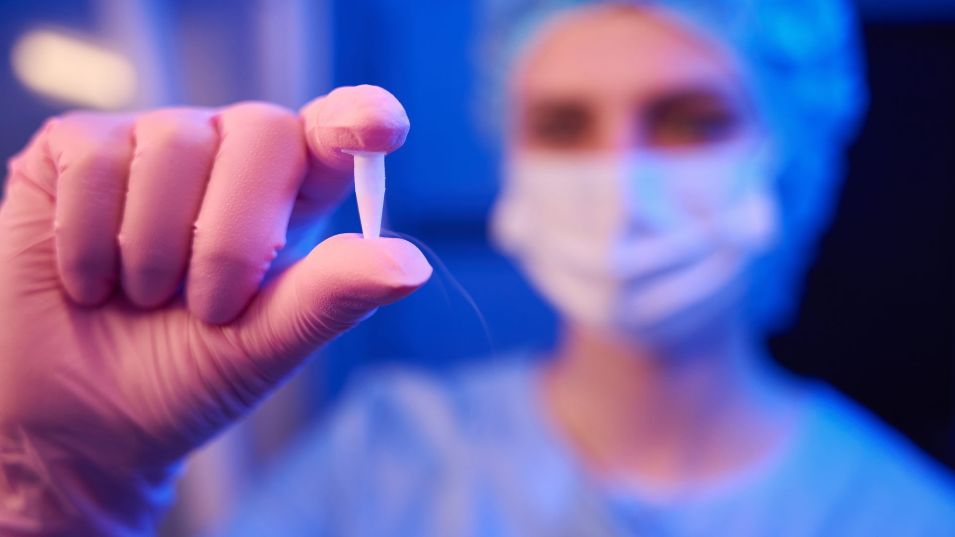 Closeup of scientist hand in sterile glove holding sealed cryogenic vial with frozen human embryos