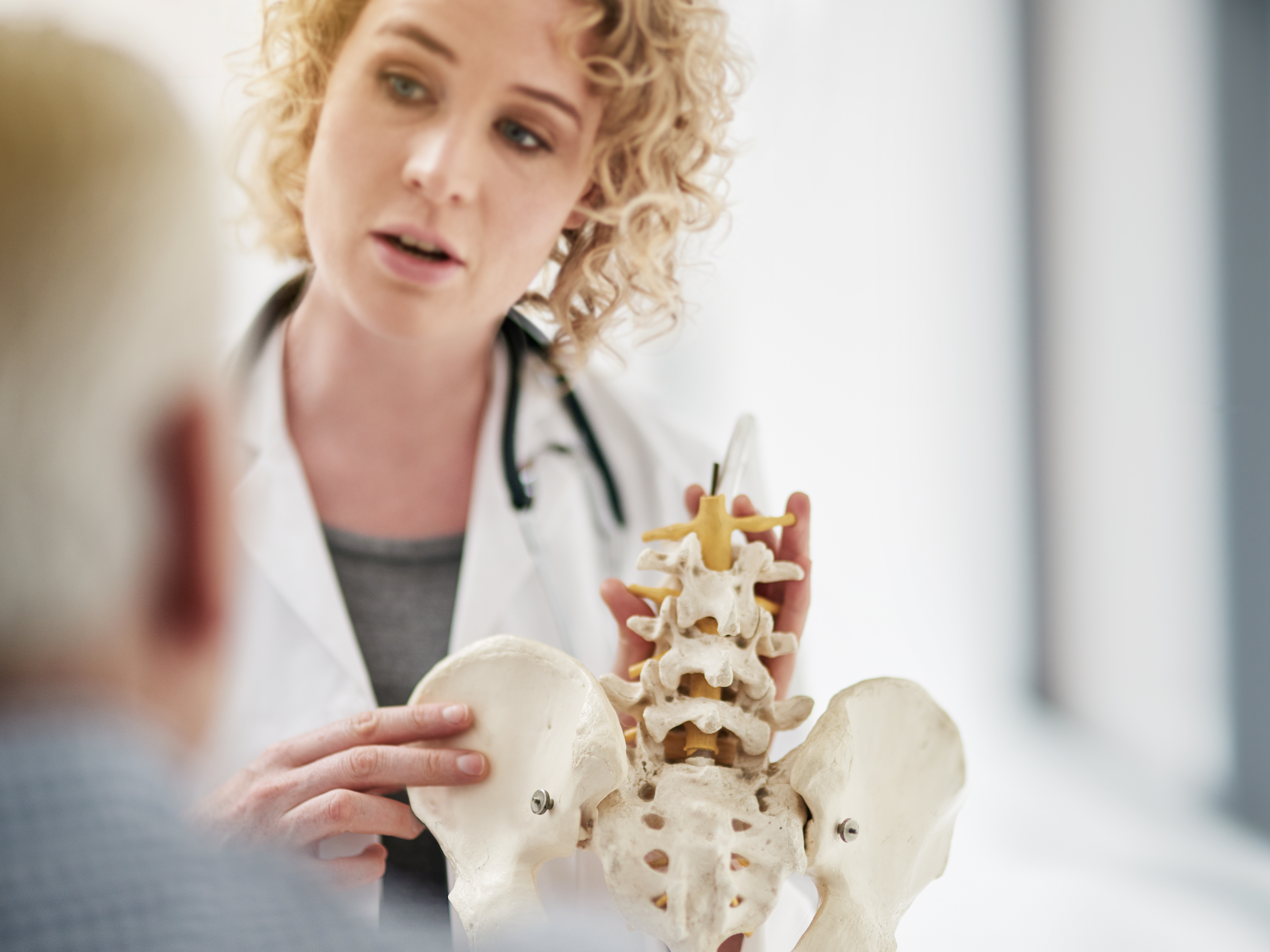 Doctor explaining a medical procedure with a model to a senior patient while sitting in her office
