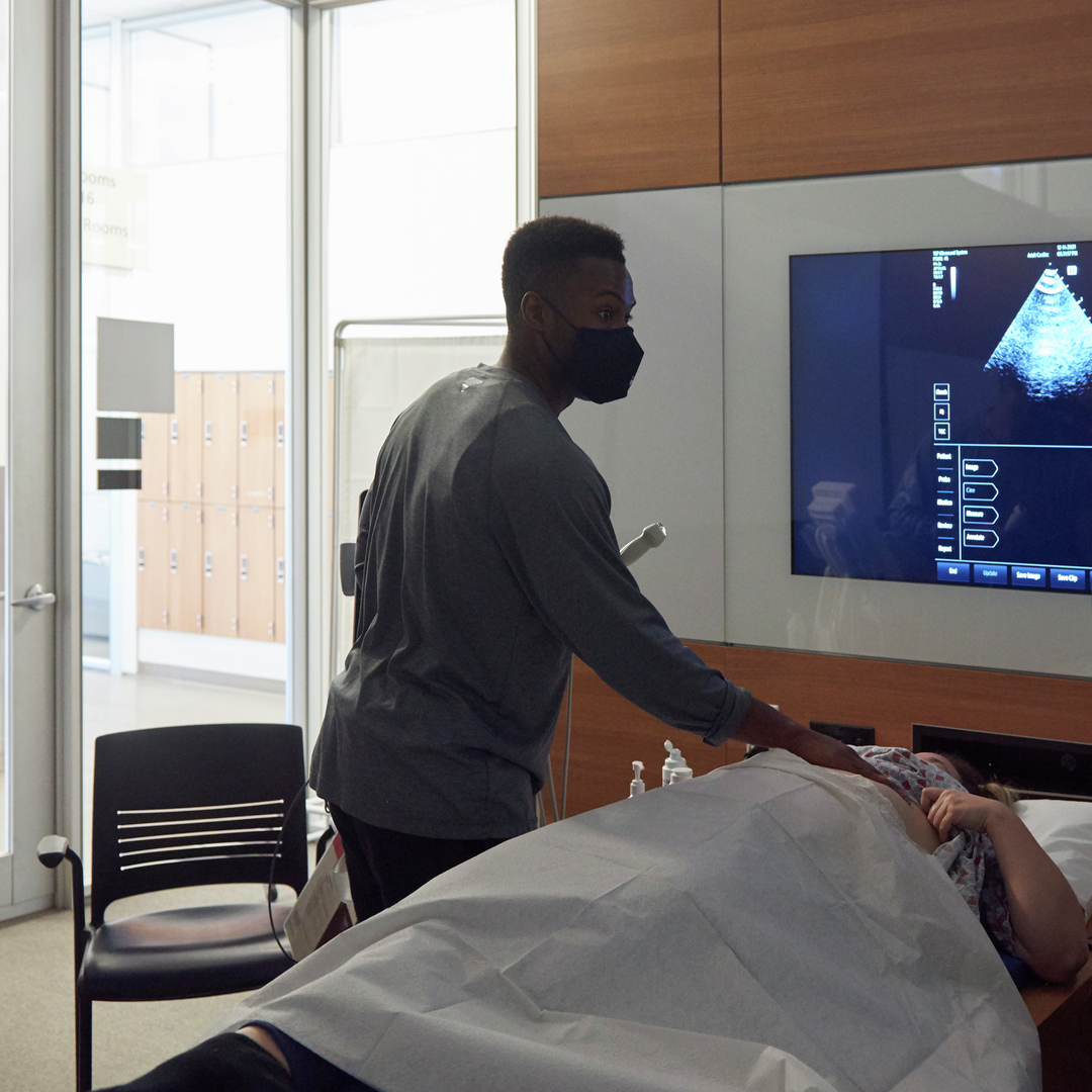 Two medical students practice using ultrasound on a volunteer in a classroom