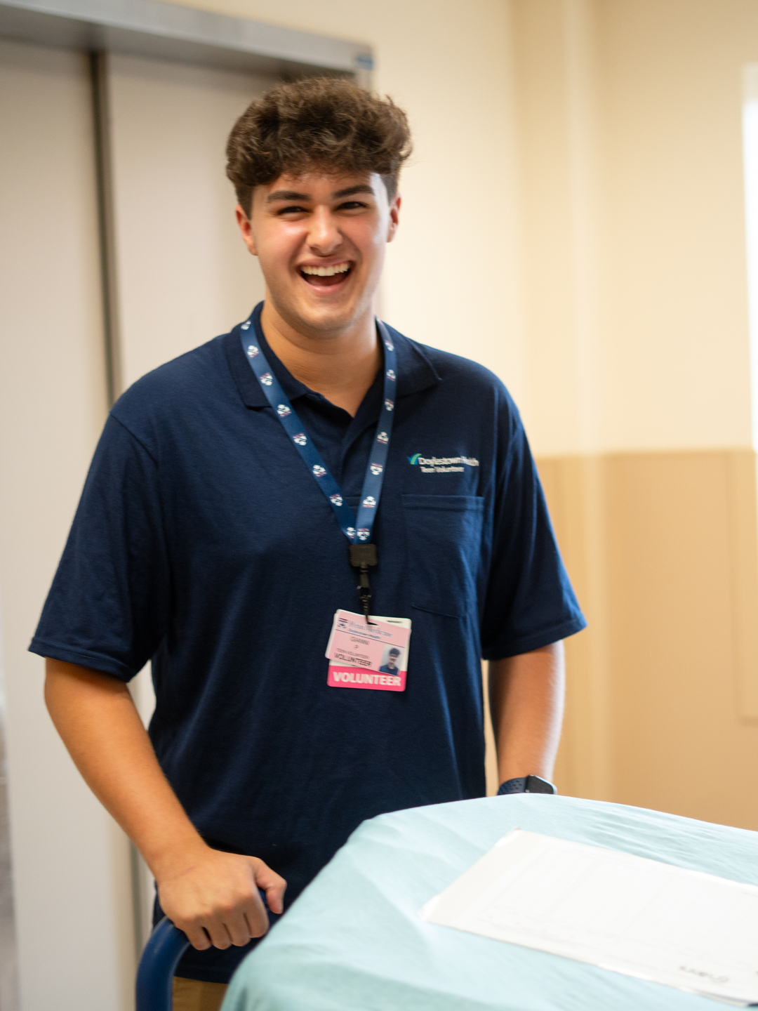 Gianni Perretta, senior at Central Bucks High School South and patient transport volunteer at Doylestown Hospital, smiles for the camera while standing behind a patient transport bed