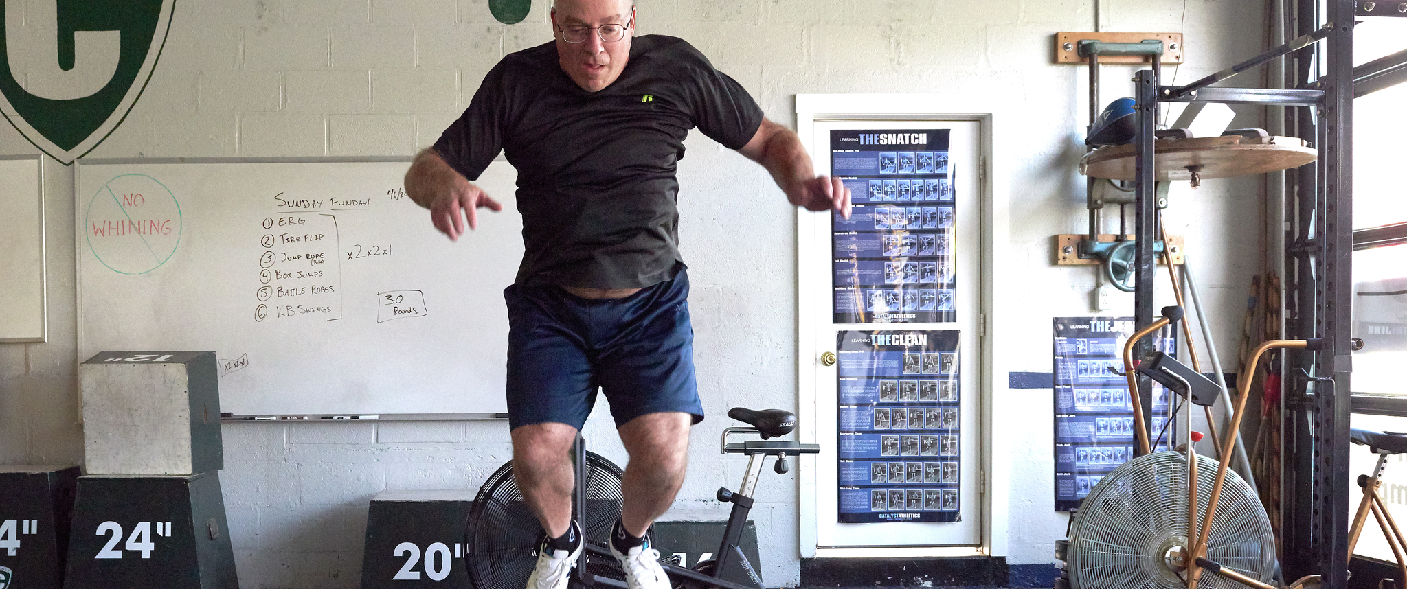 A bald man jumps vertically above a large wooden box labeled 16"