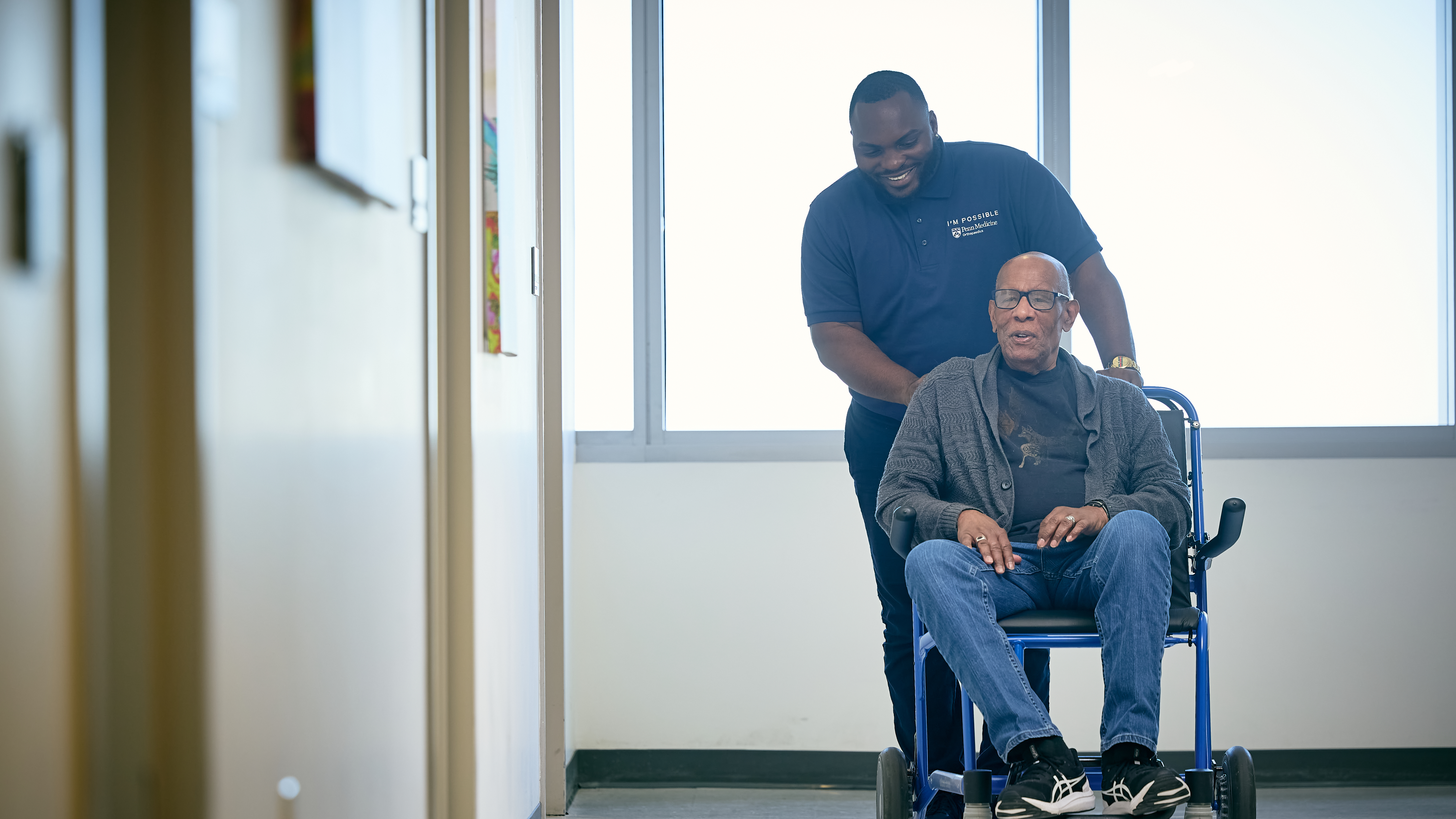 Penn Medicine employee transports orthopaedics patient in wheelchair down a hallway.