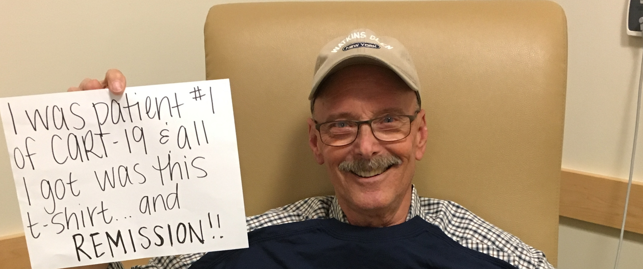 Bill Ludwig holds sign saying I was patient #1 of CART-19 & all I got was this lousy T-shirt...and remission! Wearing a shirt with a Carl June quote