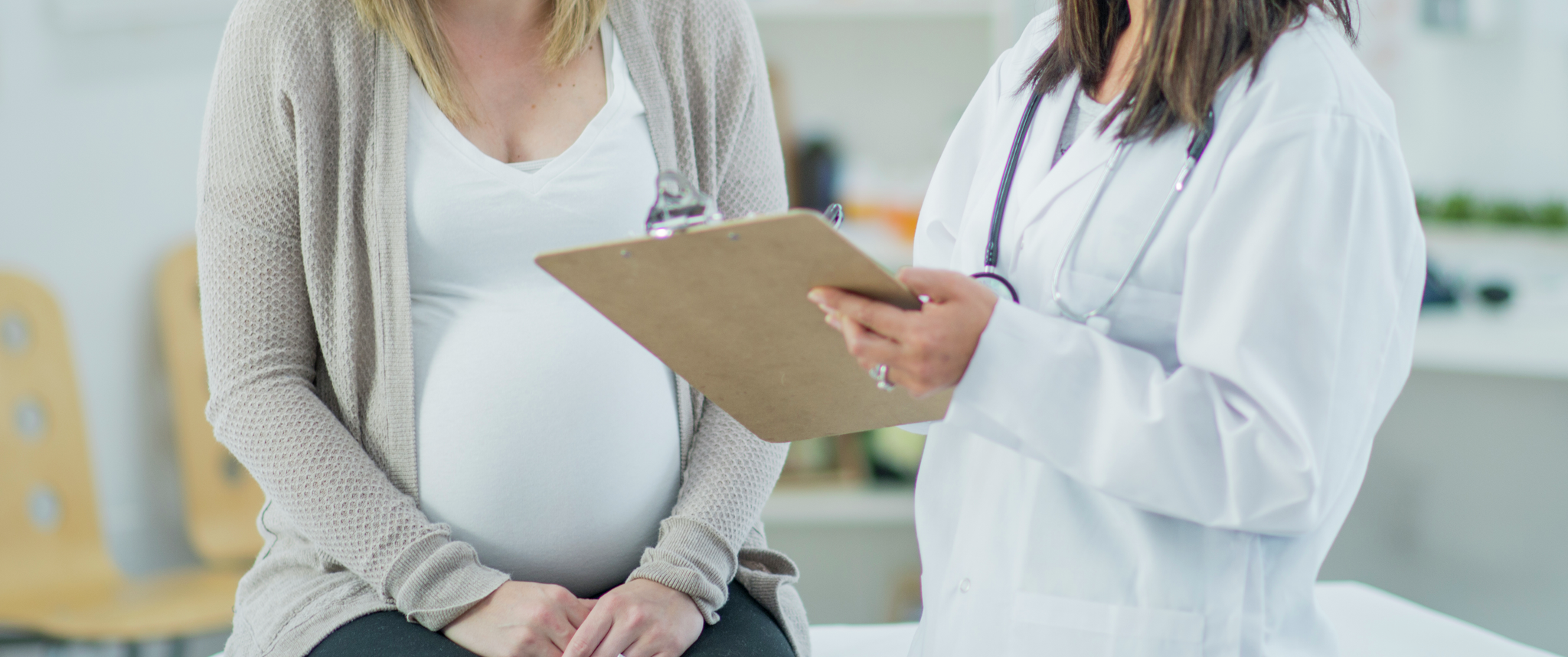 Pregnant woman with doctor holding a clipboard and giving the results of the checkup.