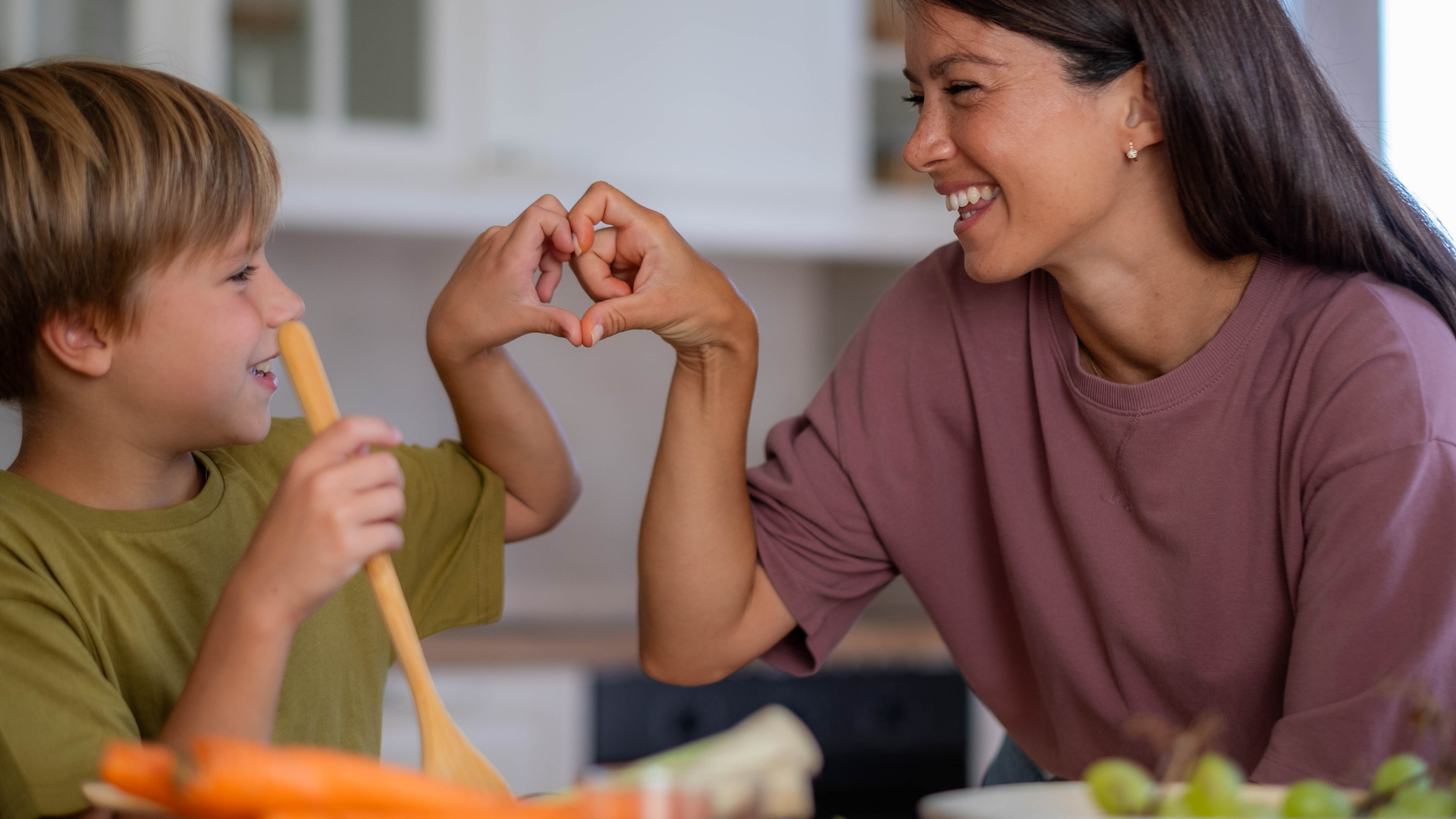 Happy mom and son in the kitchen preparing food and making a heart shape with their hands