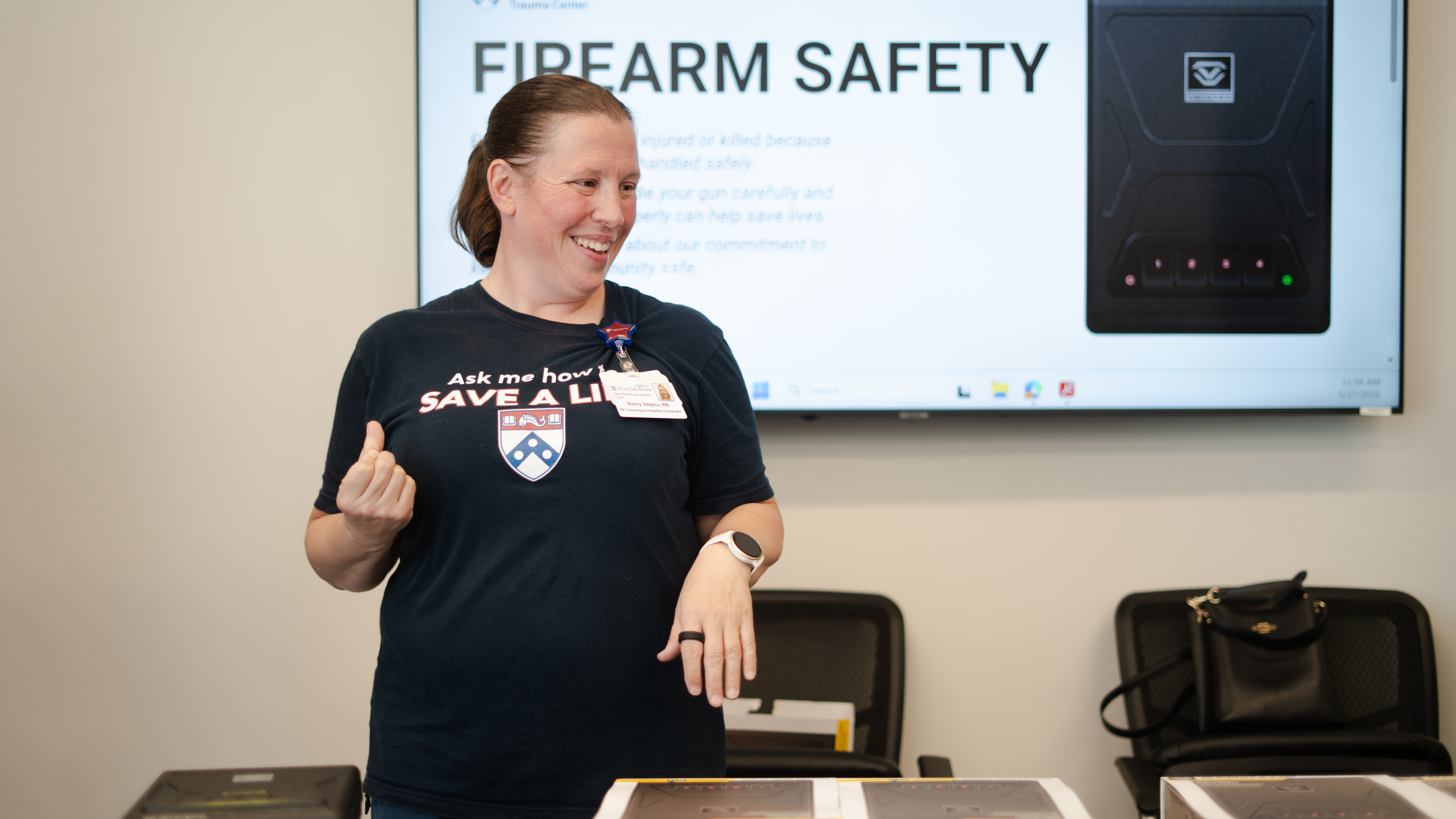 Sunny Vespico stands smiling behind a table holding several gun safes in boxes at a handout event in Delaware County.
