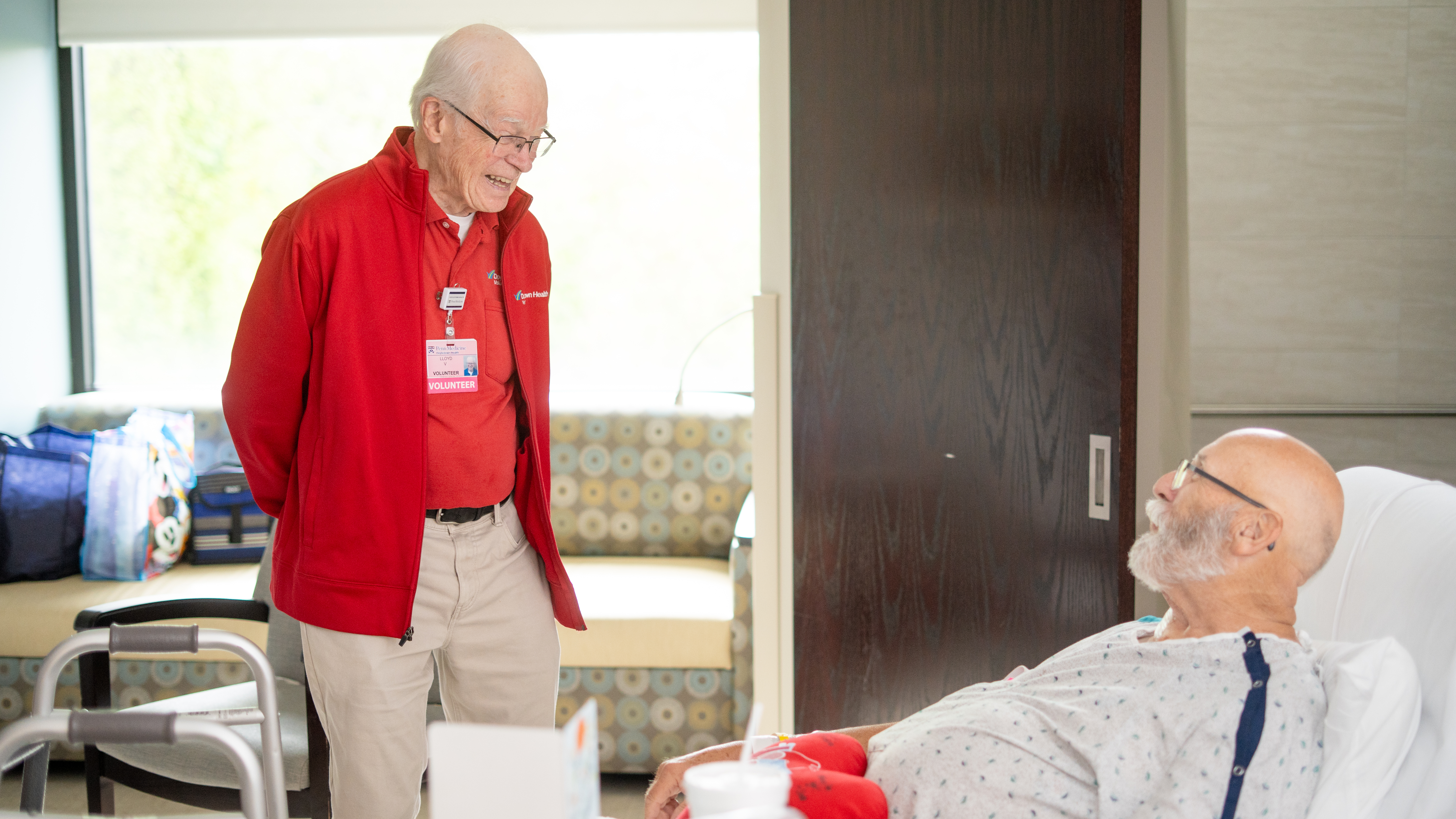 Lloyd Vansant is standing speaking with James Myers while he is laying in his bed in his hospital room