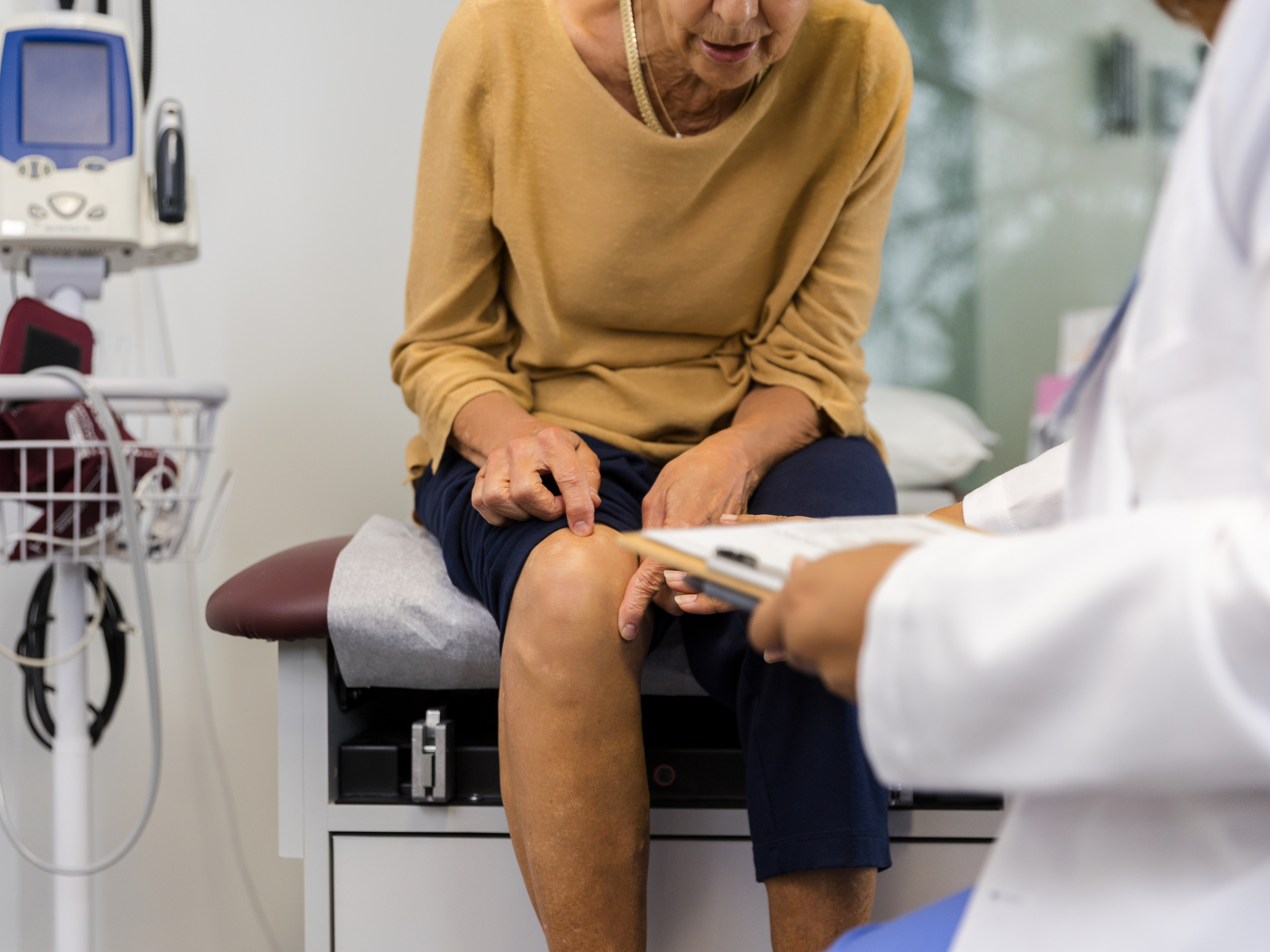 Senior woman points to knee pain during doctor's visit.