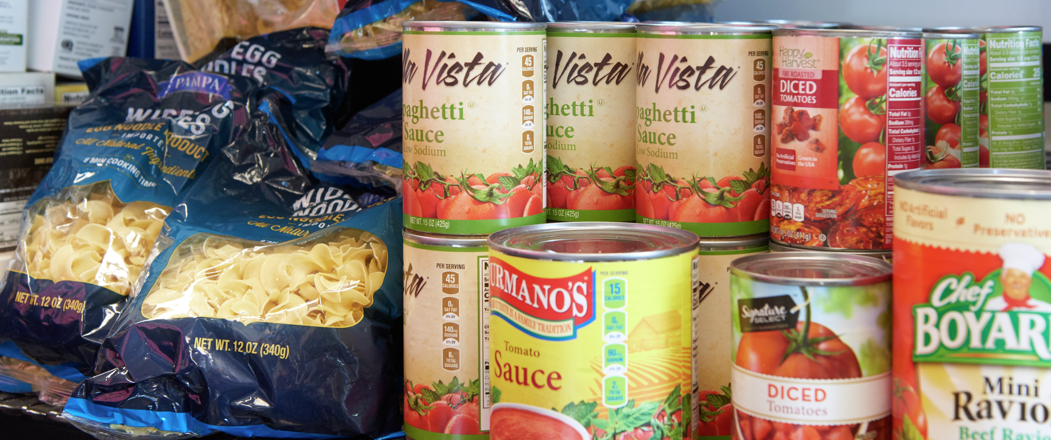 A shelf full of pantry foods including pasta and cans of tomatoes and sauce