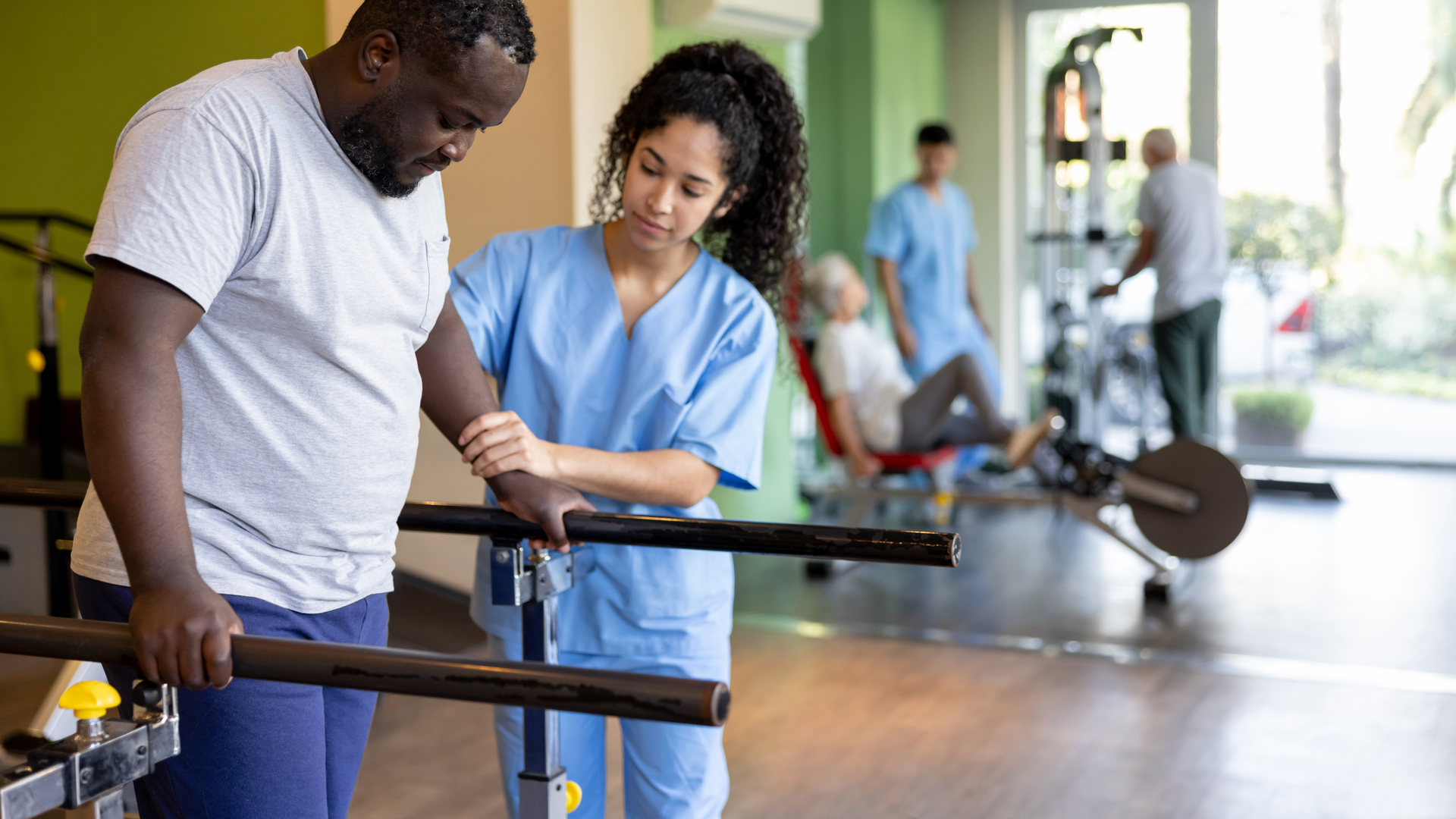 Mature man in physical therapy walking on the bars with the help of his therapist