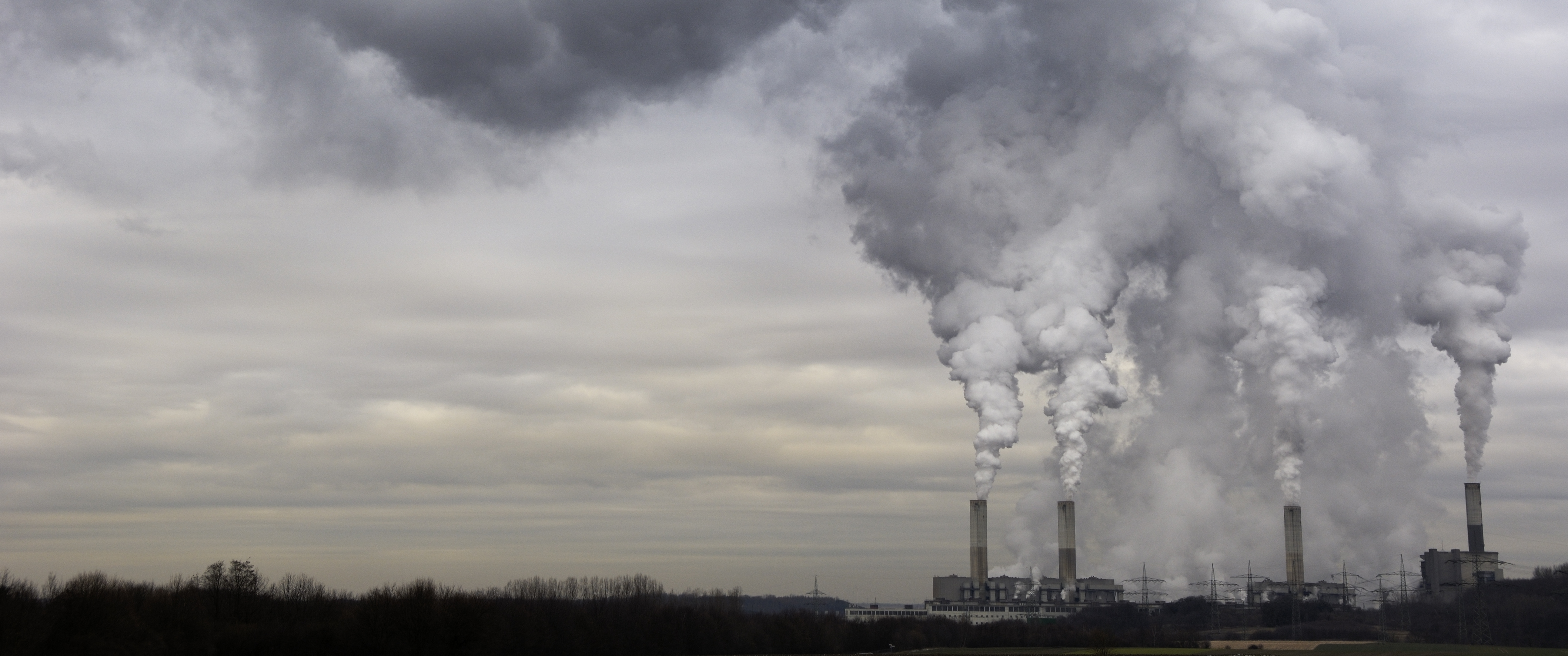 Industrial facility with multiple smokestacks releasing thick smoke.