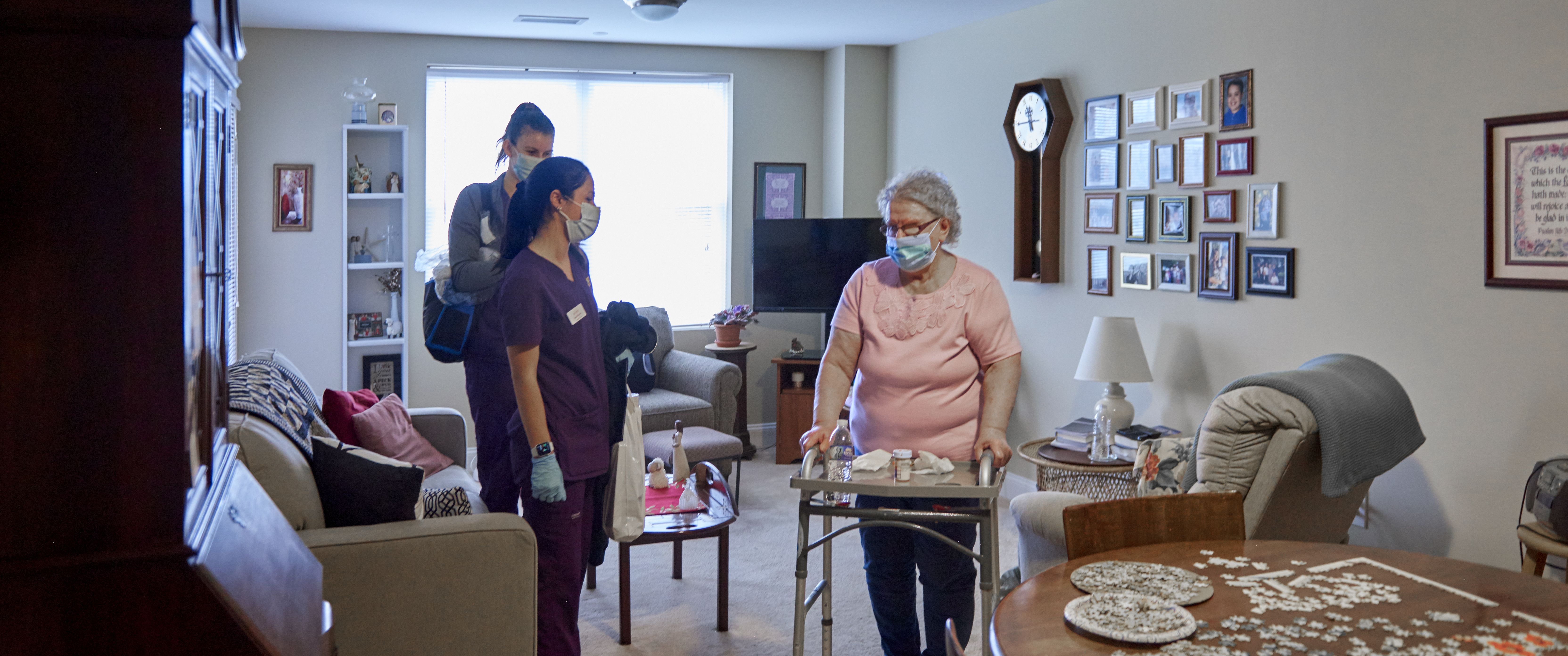 Two student nurses with an elderly woman standing with a walker in her living room