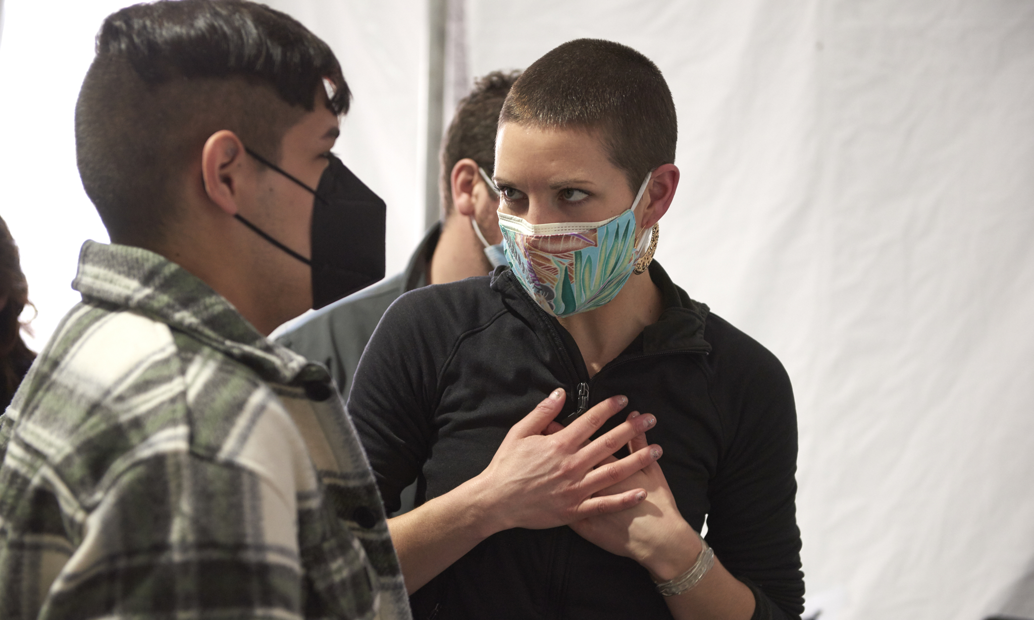 Rachel McFadden holds her hands over her heart while speaking with another masked person