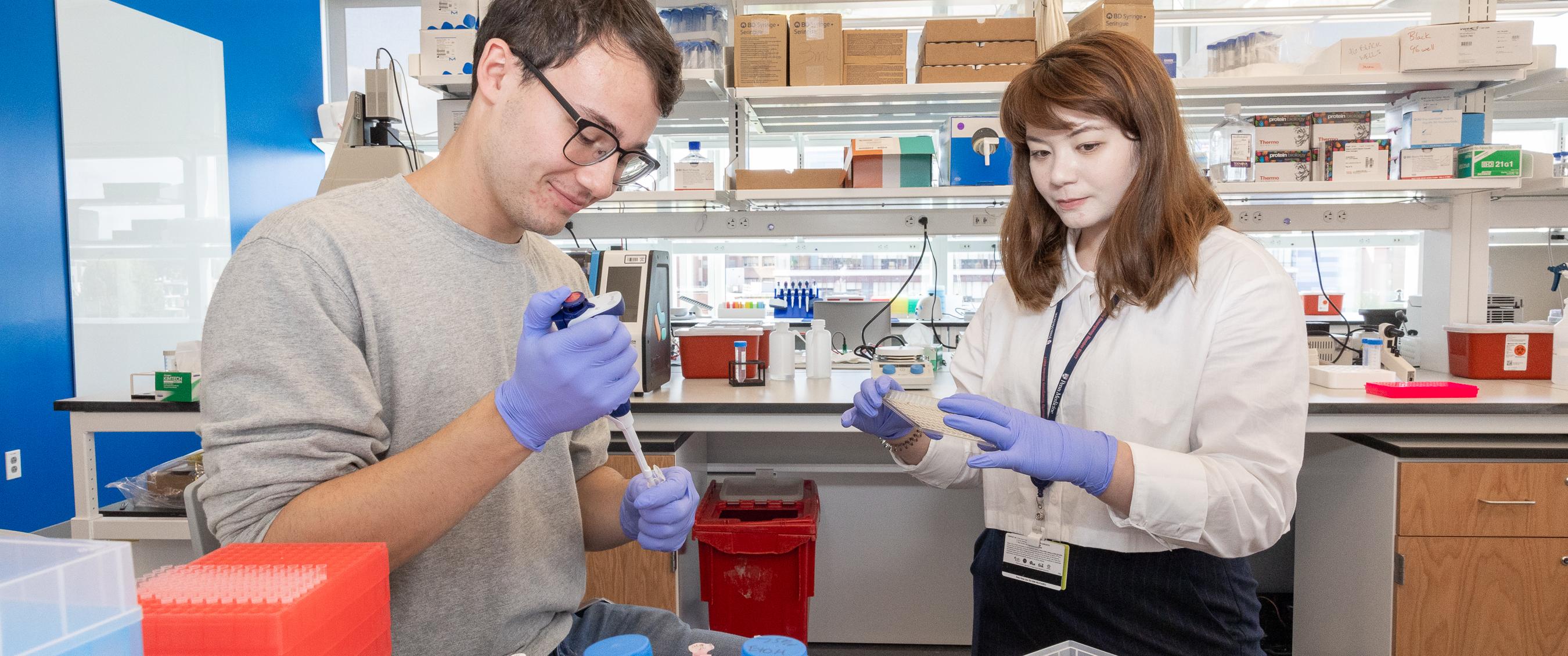 A man and woman hold lab equipment while doing research with mRNA
