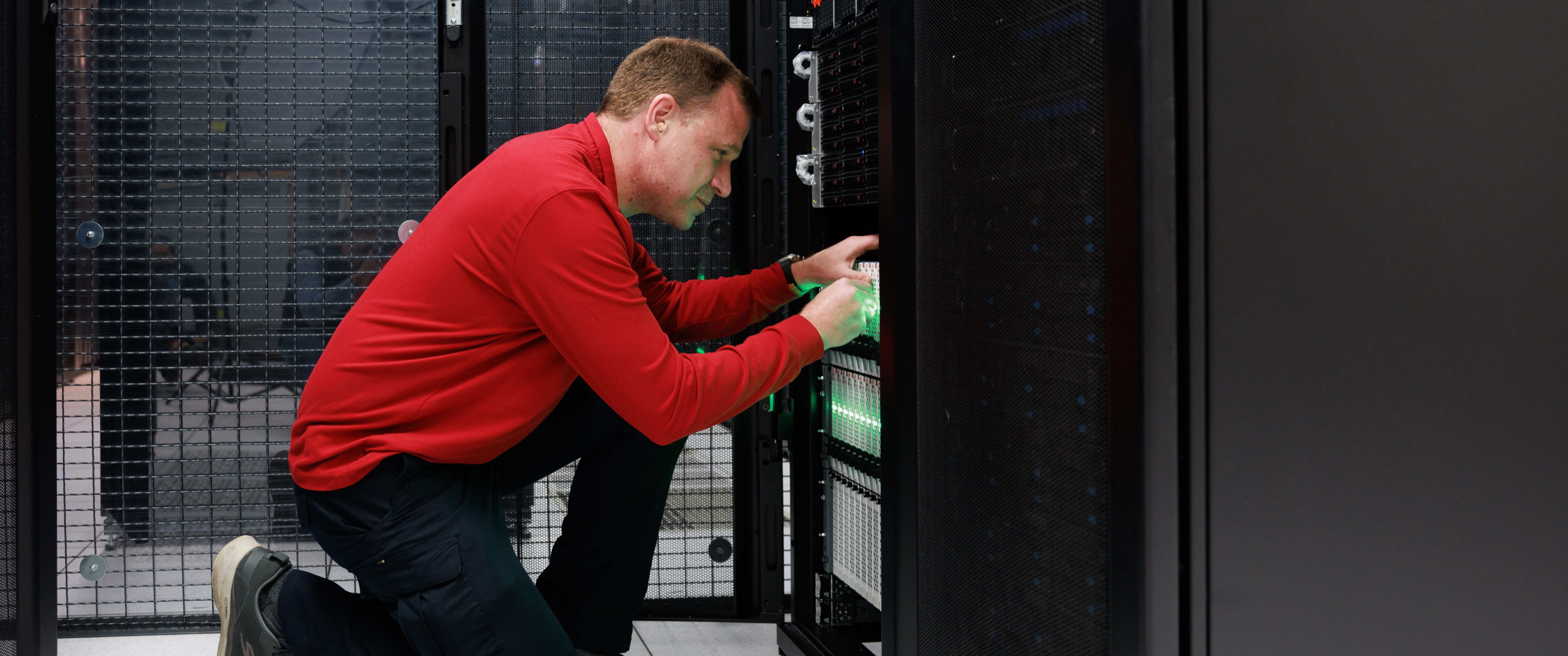 Gregory Bowman, kneeling in a data center, reaching hands in touching a computer server