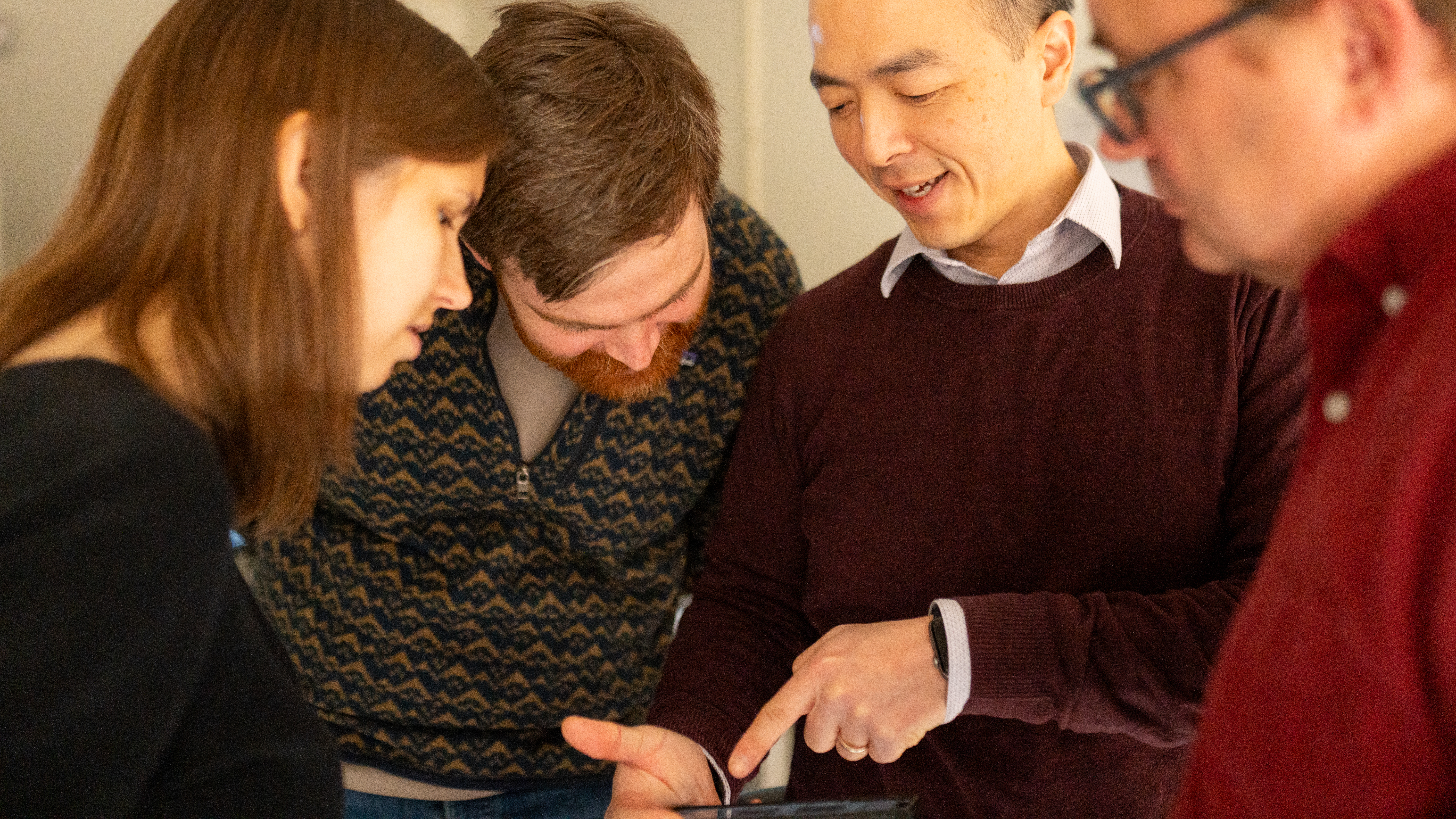 Kathryn Kixmoeller, Benjamin Creekmore, Yi-Wei Chang, and Ben Black all lean in to look at an image in a phone held by Chang