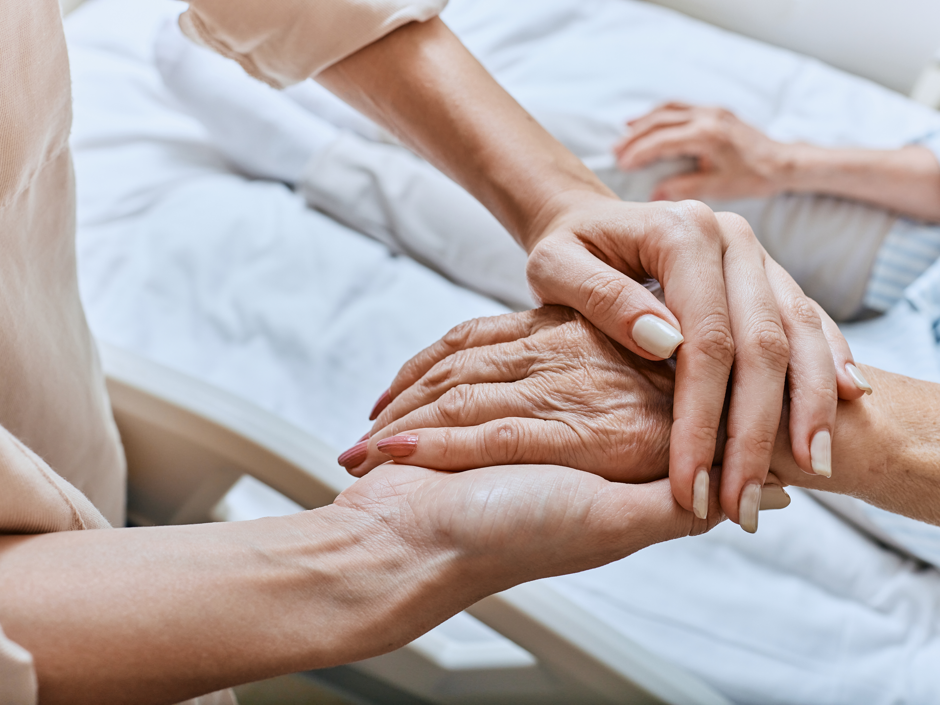 Relative holding trembling hand of senior woman with Parkinson's disease lying in hospital bed at medical ward. 